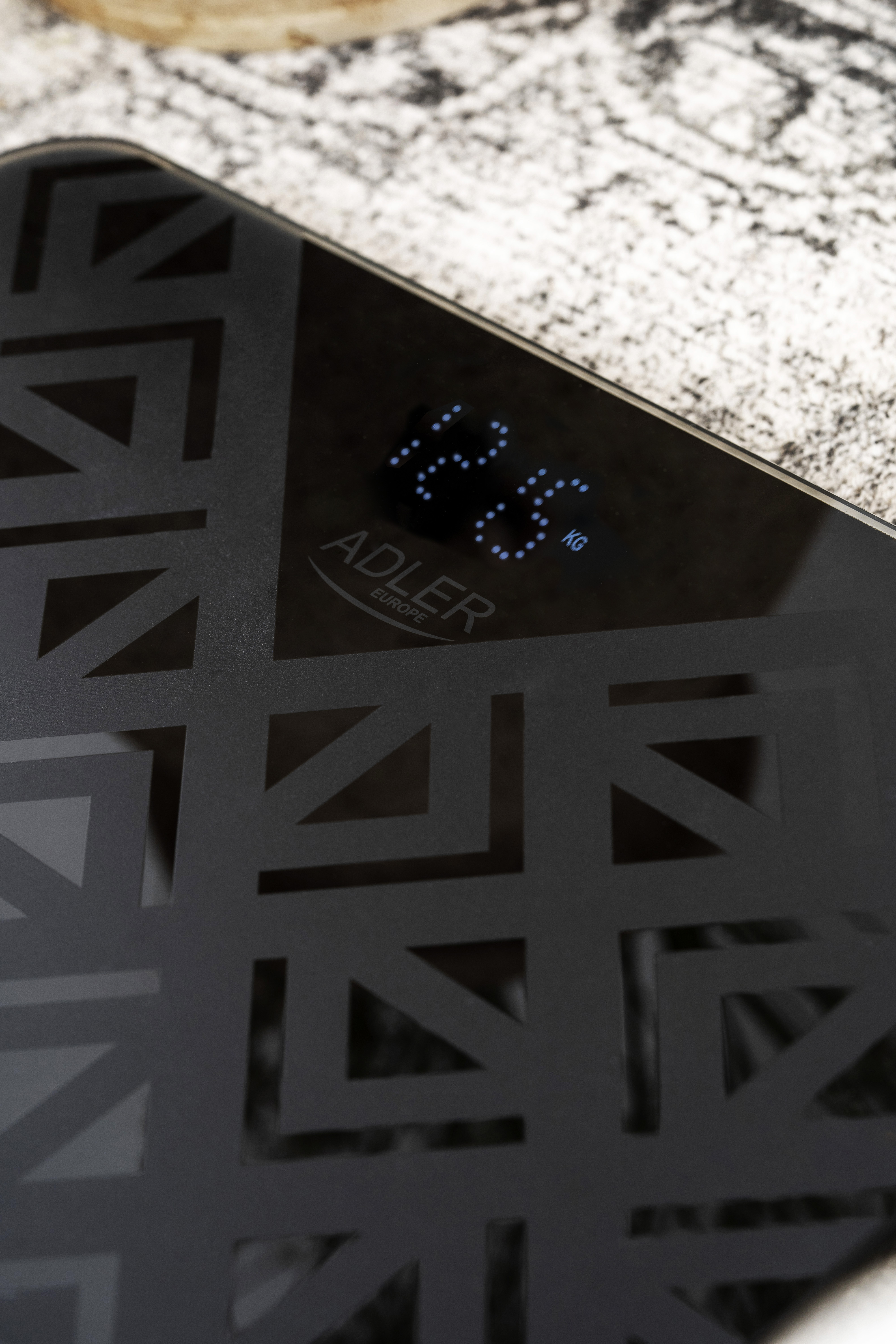 Zbliżenie czarnej wagi łazienkowej z wzorzystą powierzchnią, pokazujące 12,8 kg.