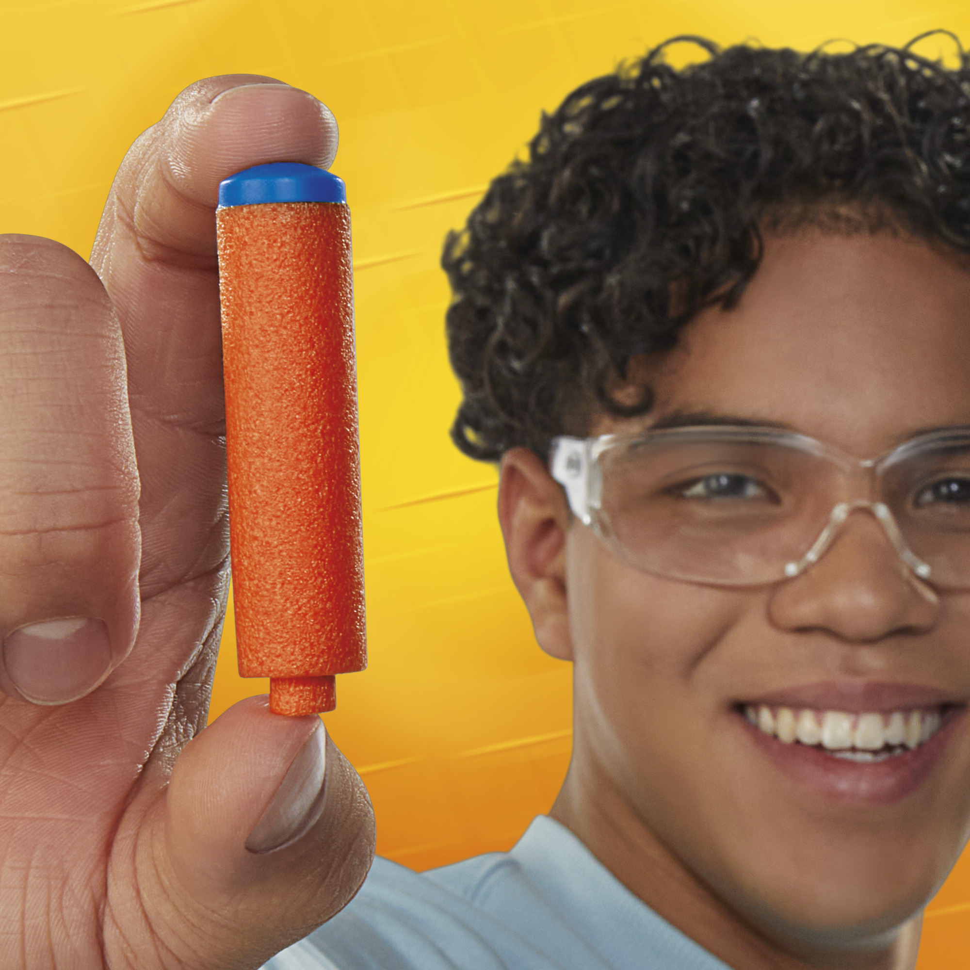 Un joven sostiene un dardo Nerf naranja y azul. Lleva gafas de seguridad.
