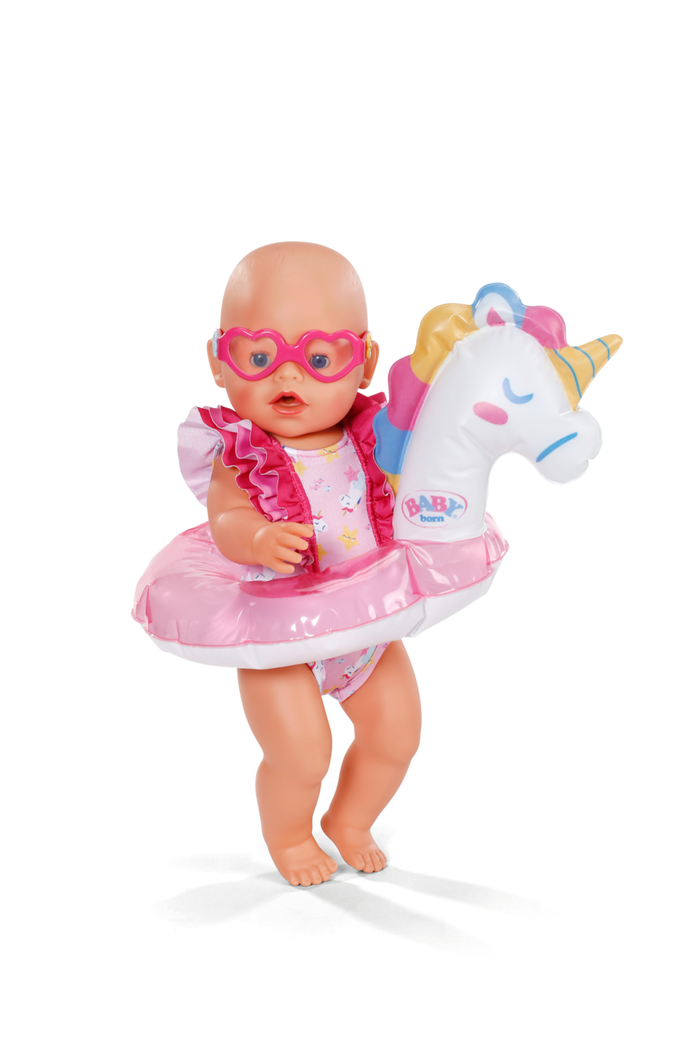Lalka Baby Born w różowych okularach przeciwsłonecznych w kształcie serca i jednorożec na białym tle.