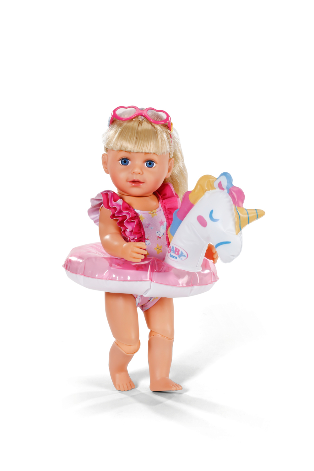 Lalka Baby Born z blond włosami, okularami przeciwsłonecznymi w kształcie serca i jednorożcem na białym tle.