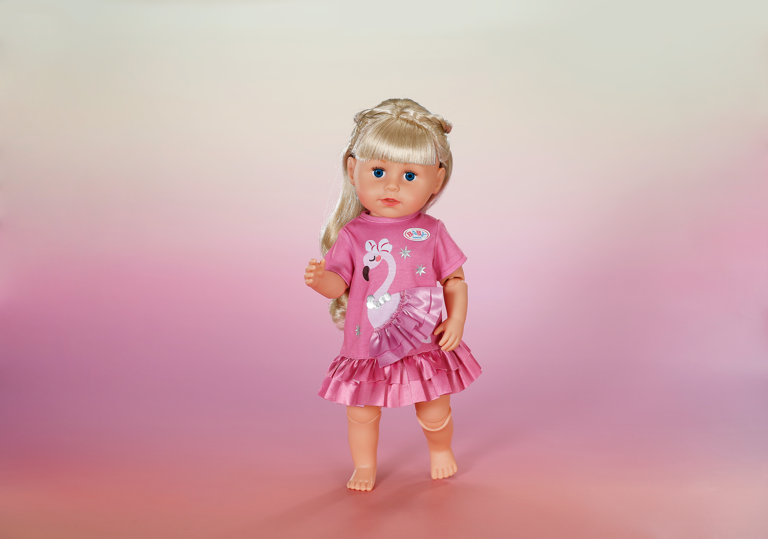 Lalka z blond włosami w różowej sukience z flamingiem na różowym tle.
