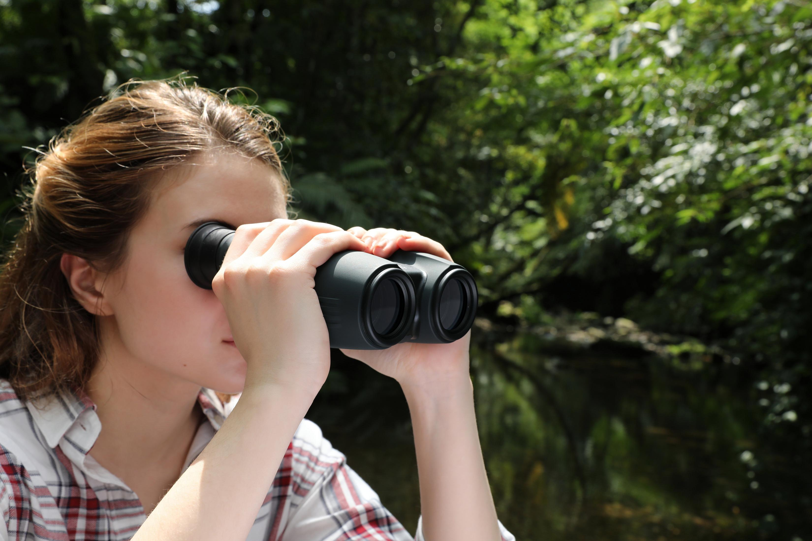 Kobieta używa lornetki, patrząc na jezioro. Zielone tło, mała głębia ostrości, naturalne światło.