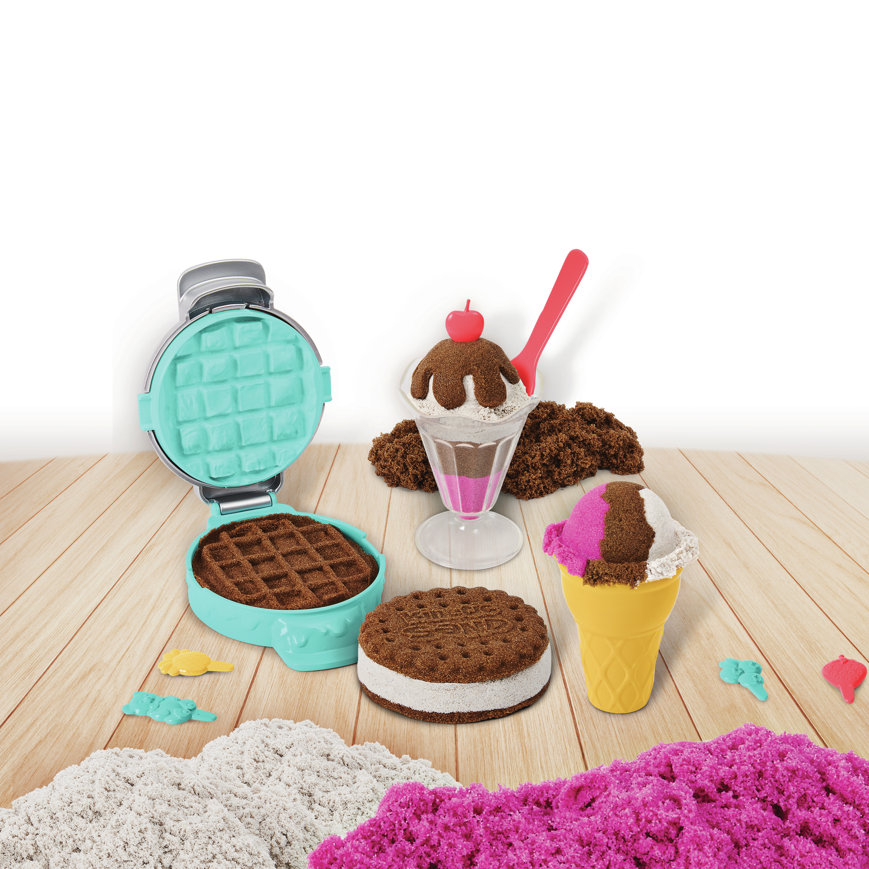 Arte de arena con máquina de gofres, helado y conos, sobre una mesa de madera con arena rosa y blanca.