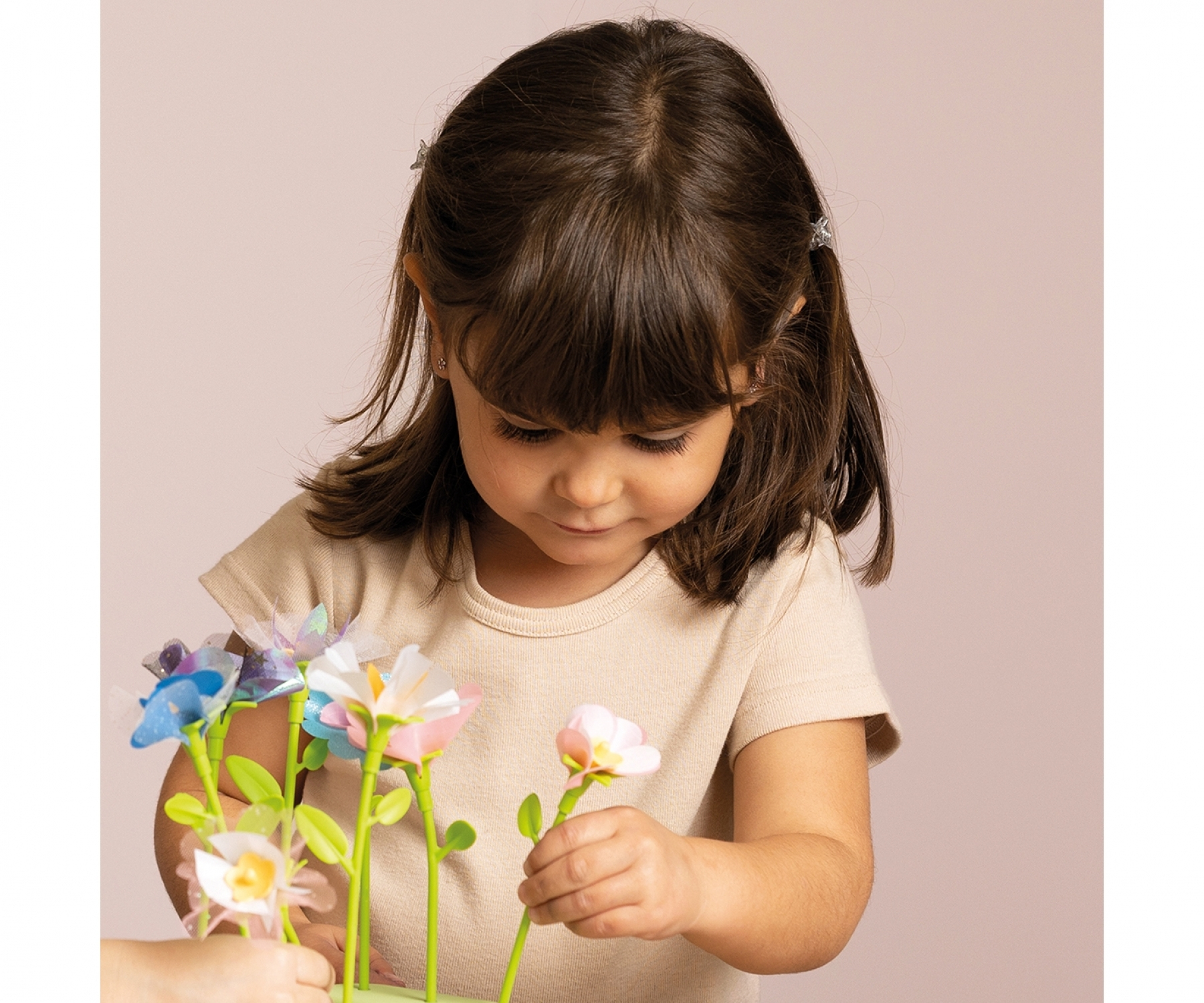 Mała dziewczynka w beżowej koszuli patrzy na zestaw papierowych kwiatów, trzymając jeden w ręku.
