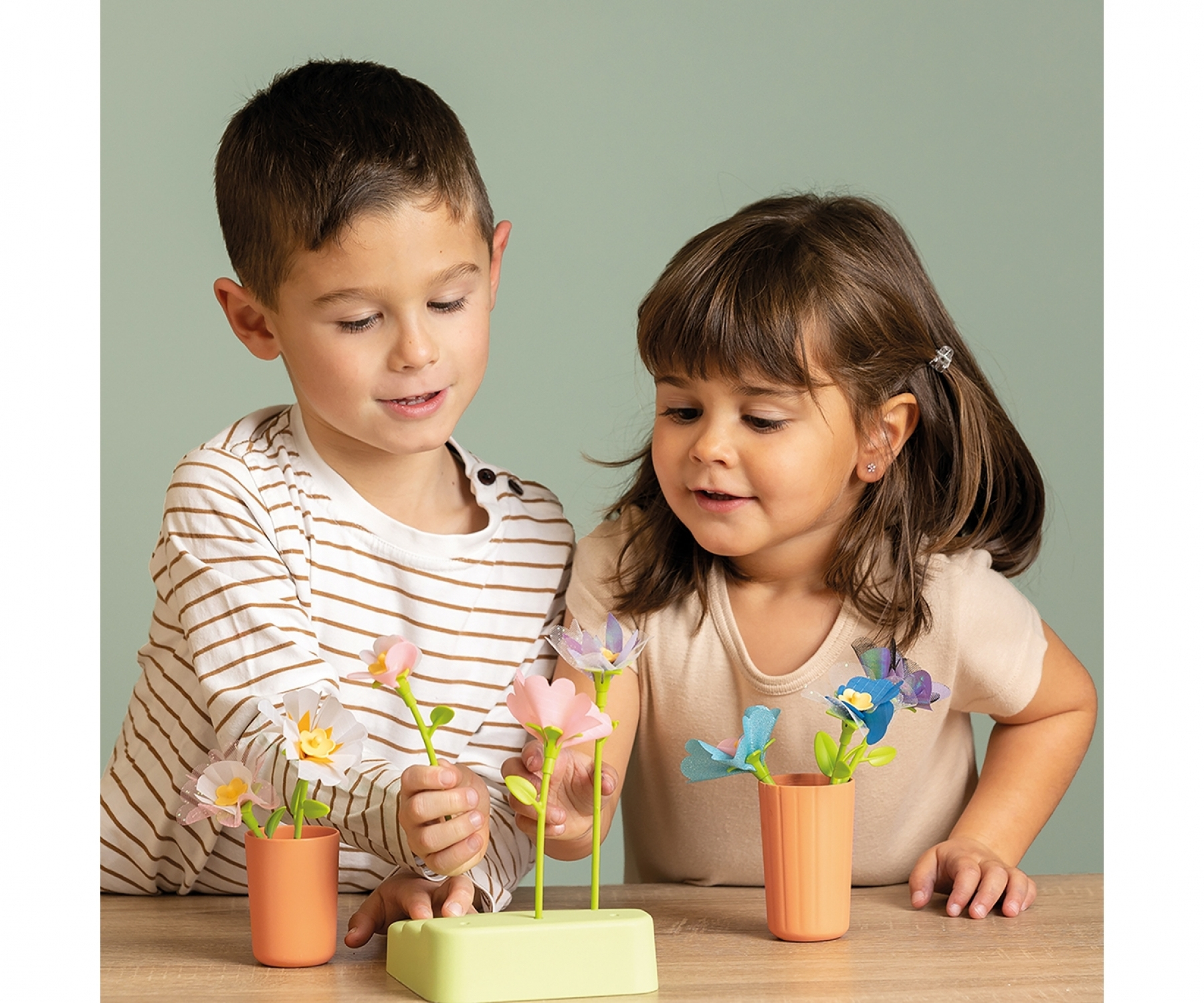 Dwoje dzieci bawiących się kwiatami. Jeden chłopiec i jedna dziewczynka. Uśmiechają się.