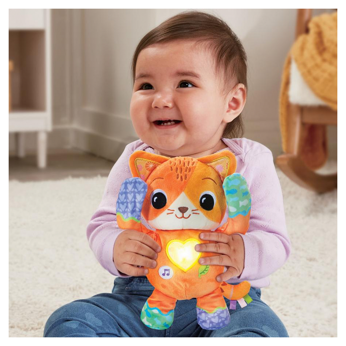 Ein Baby hält eine orangefarbene Spielzeugkatze und lächelt glücklich, in häuslicher Umgebung.