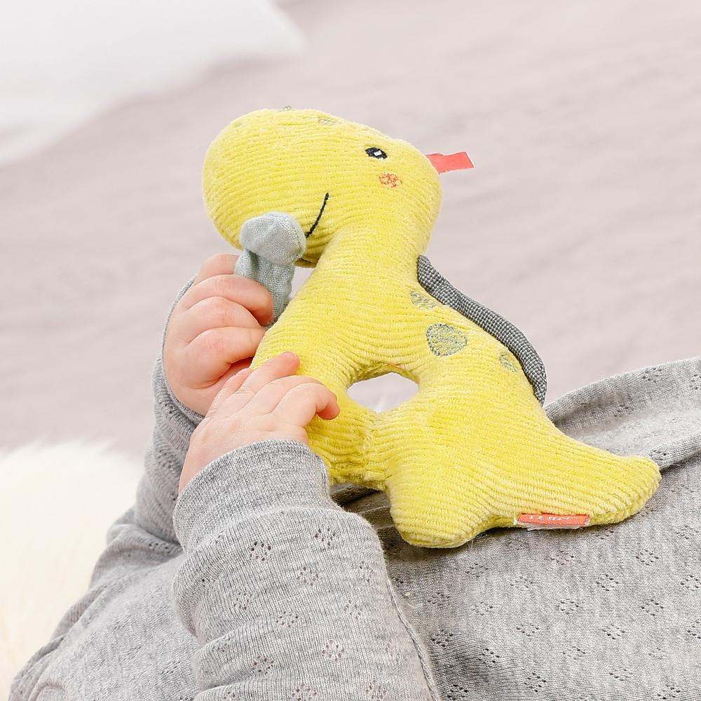 Ręce dziecka trzymające żółtą pluszową zabawkę dinozaura. Szary sweter i tło.