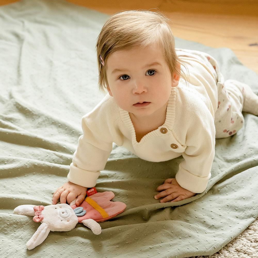 Baby auf einer Decke mit einem Plüschtier, das in die Kamera schaut.