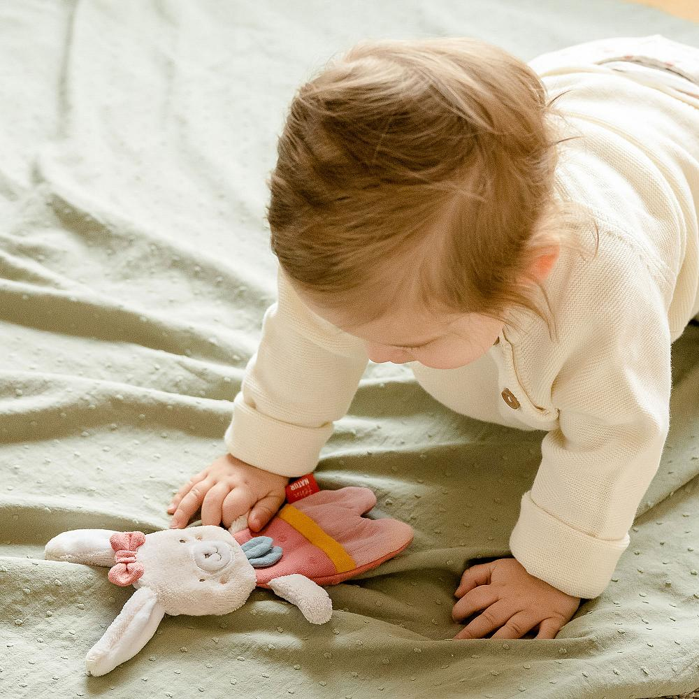 Ein Baby krabbelt auf einer grünen Decke mit einem kleinen Häschen-Spielzeug davor.