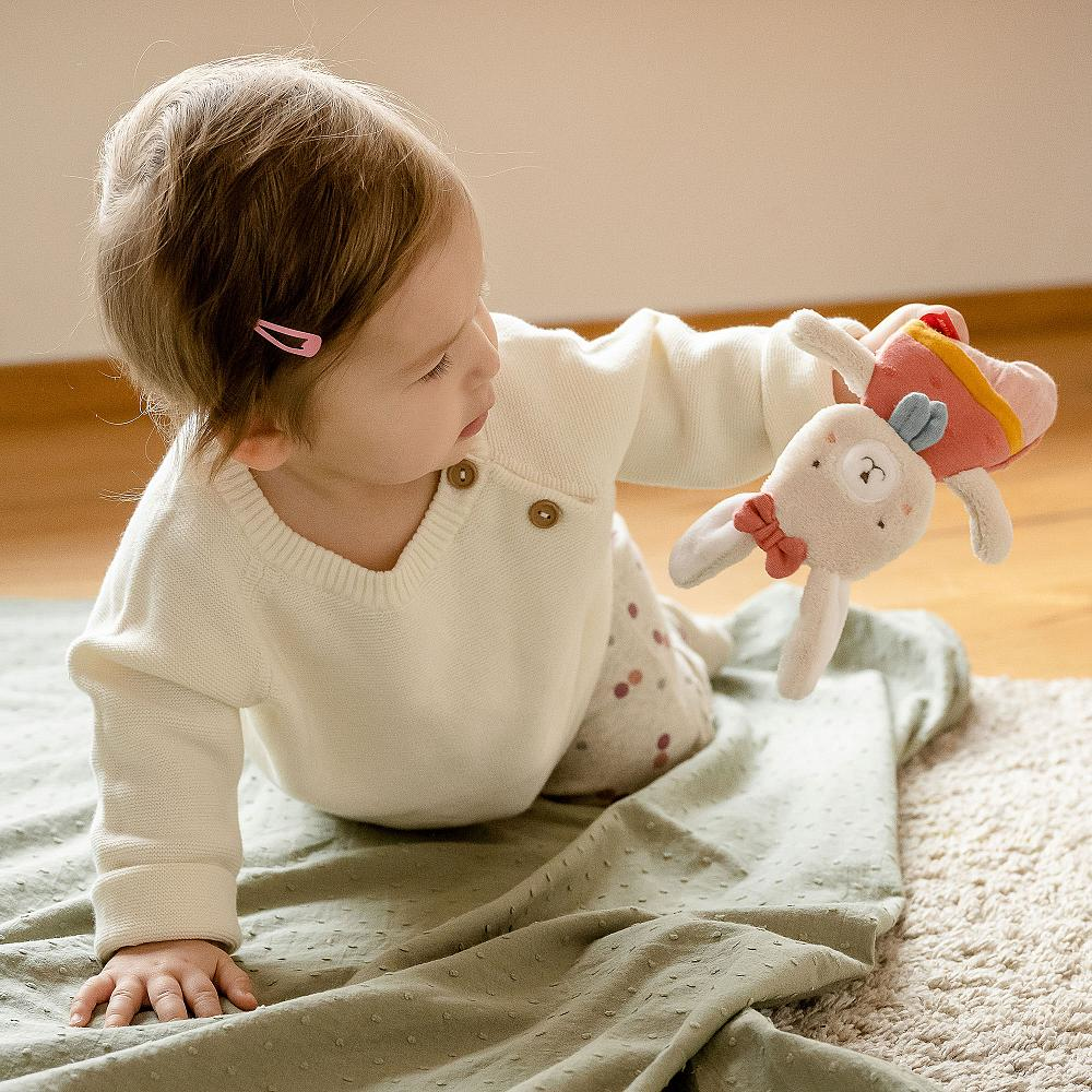 Baby spielt mit einem Spielzeug auf einer Decke und schaut sich das Spielzeug an.