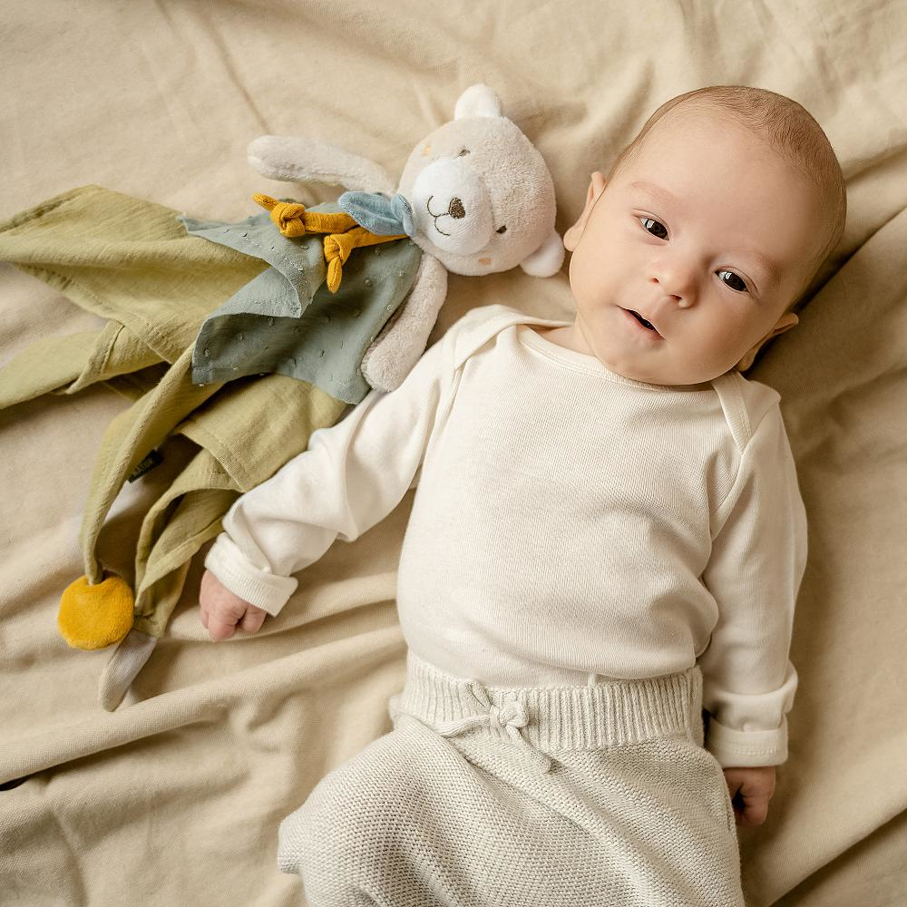 Niemowlę leżące na kocu z zabawką. Dziecko patrzy w kamerę. Miękkie tło.