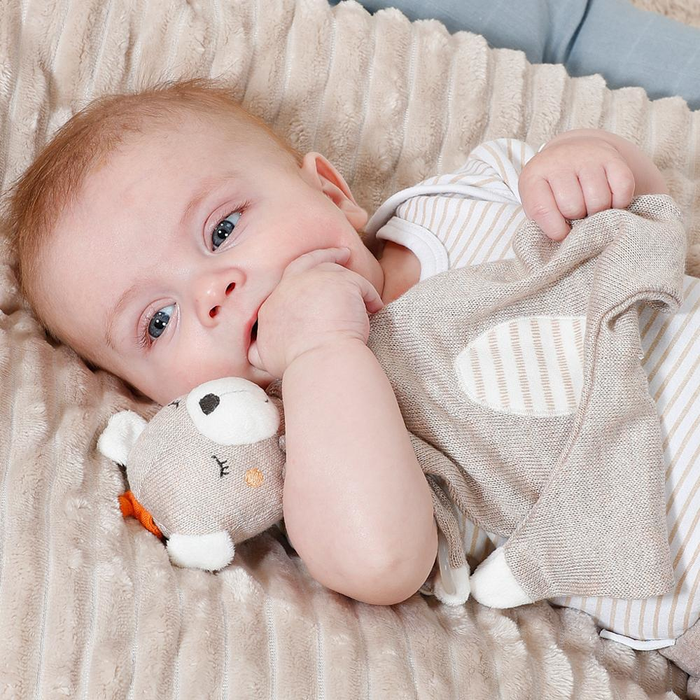 Bambino sdraiato su una soffice coperta beige, che tiene un peluche.