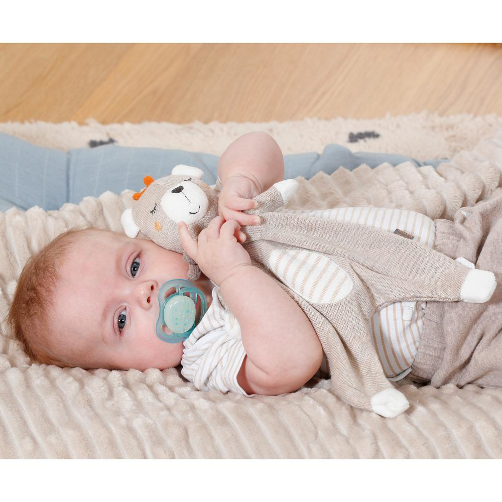 Bambino con ciuccio, sdraiato su una coperta soffice, che tiene un orsacchiotto.