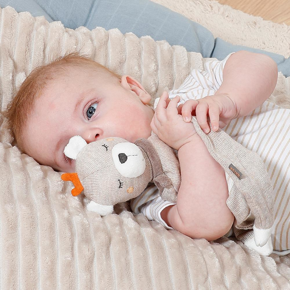 Bambino con occhi azzurri su coperta di peluche, tiene un orsetto beige.