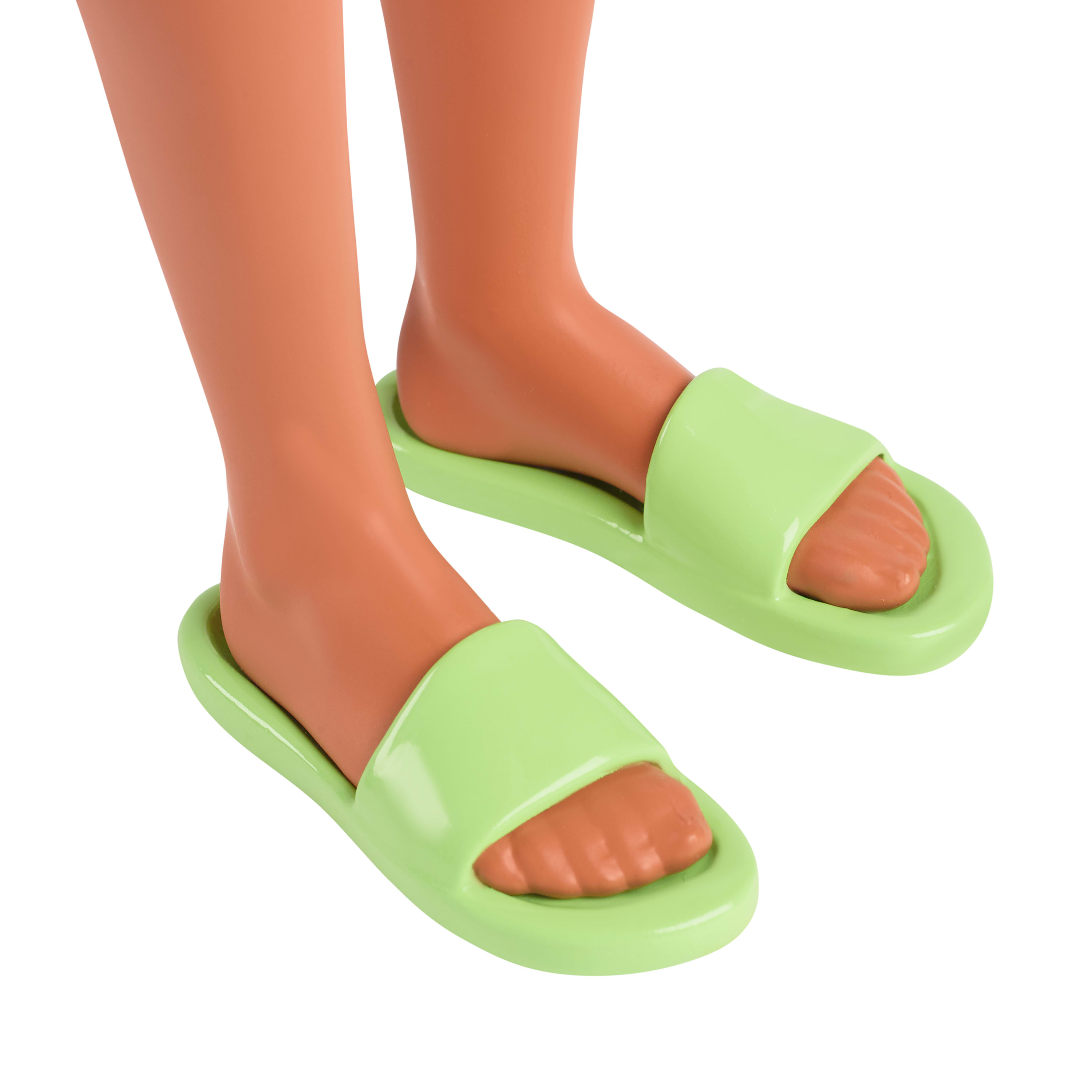 Pies de muñeca en sandalias verdes, primer plano, sobre fondo blanco.