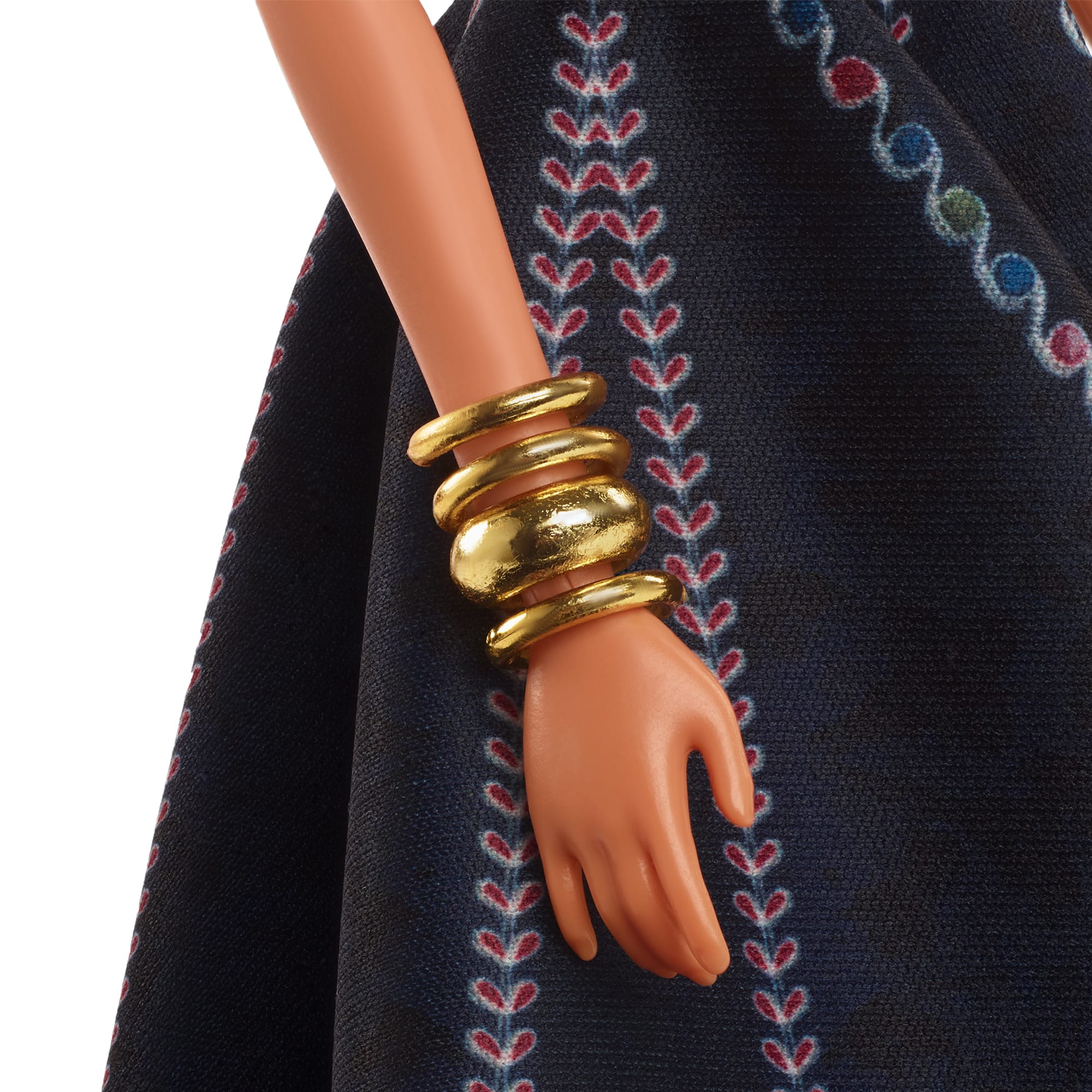 Nahaufnahme des Arms einer Barbie-Puppe mit goldenen Armbändern. Die Puppe trägt ein schwarzes Kleid.