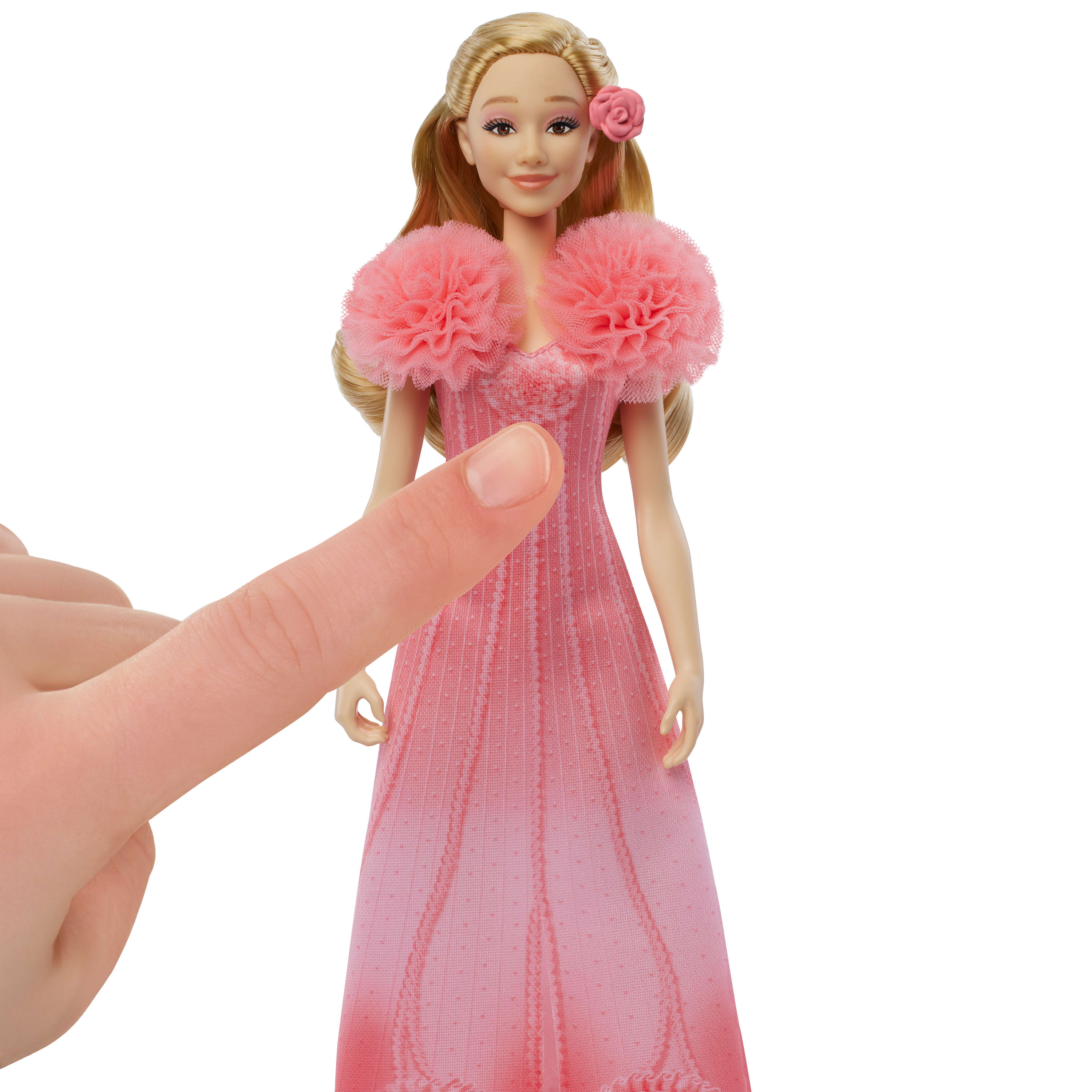 Ein Finger, der auf eine Puppe in einem rosa Kleid mit einer rosa Blume und einem rosa Pelzkragen zeigt.