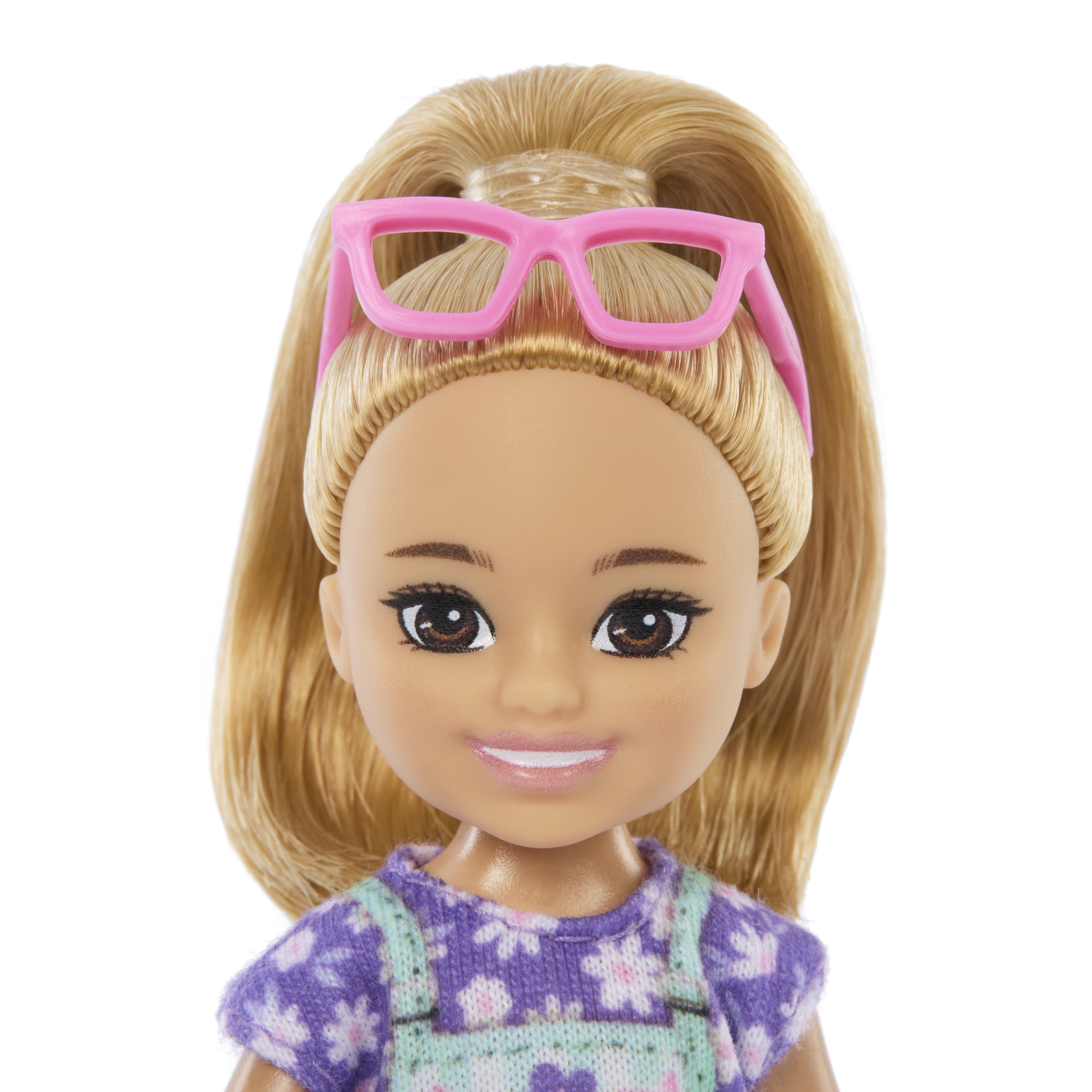 Puppe mit Pferdeschwanz und rosa Brille, lila und geblümtes Outfit, lächelt in die Kamera.