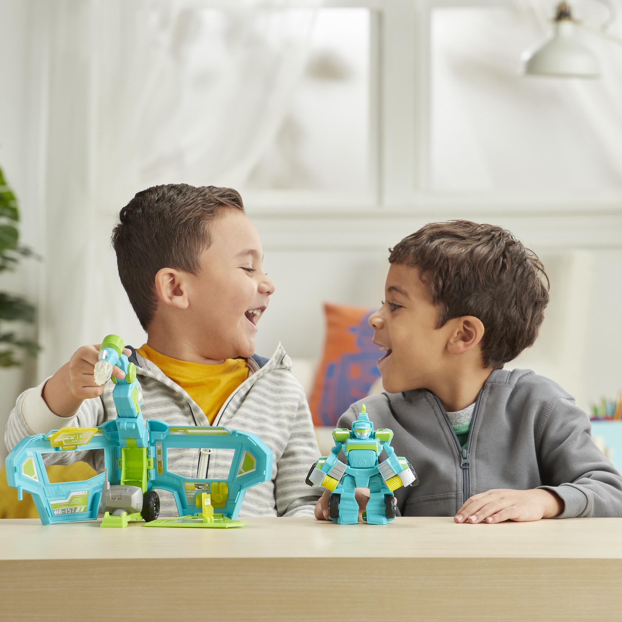 Due ragazzi si sorridono, giocattoli tra loro. Uno tiene un giocattolo blu e verde. L'altro ha un robot.