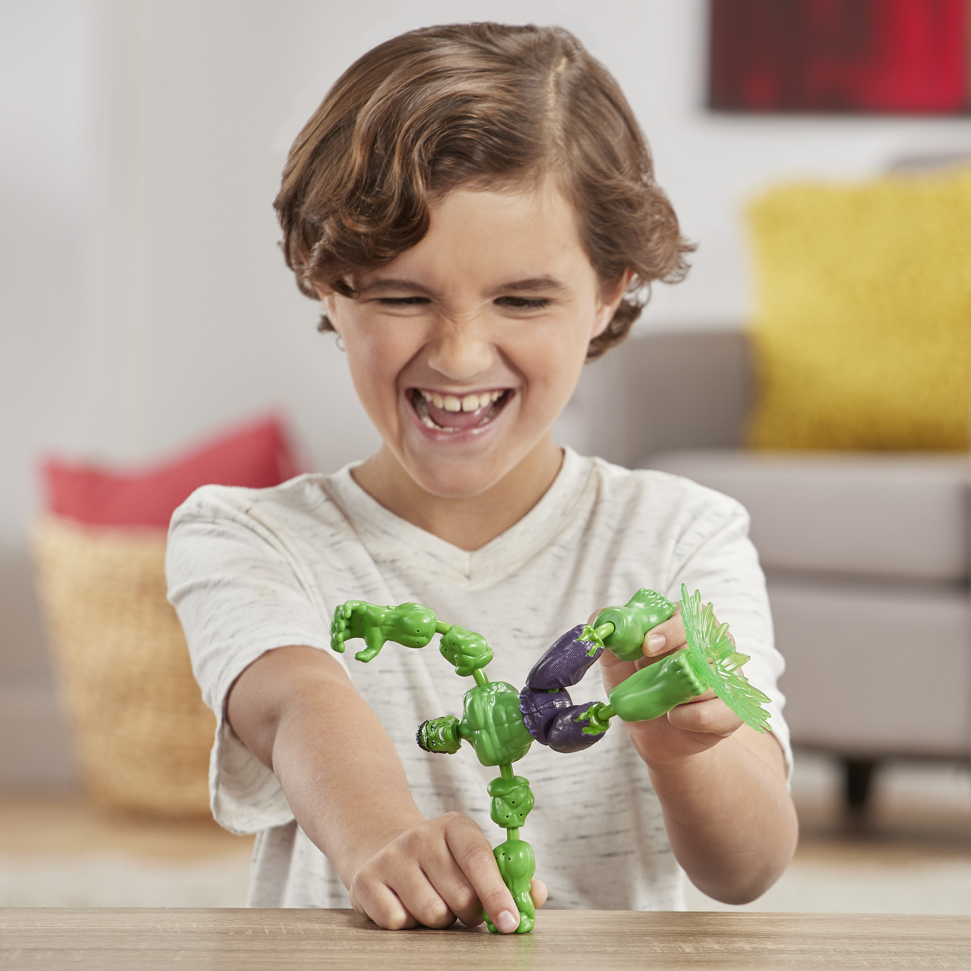 Bambino gioca con un giocattolo di Hulk, il giocattolo è parzialmente assemblato, sorridente, su un tavolo di legno.