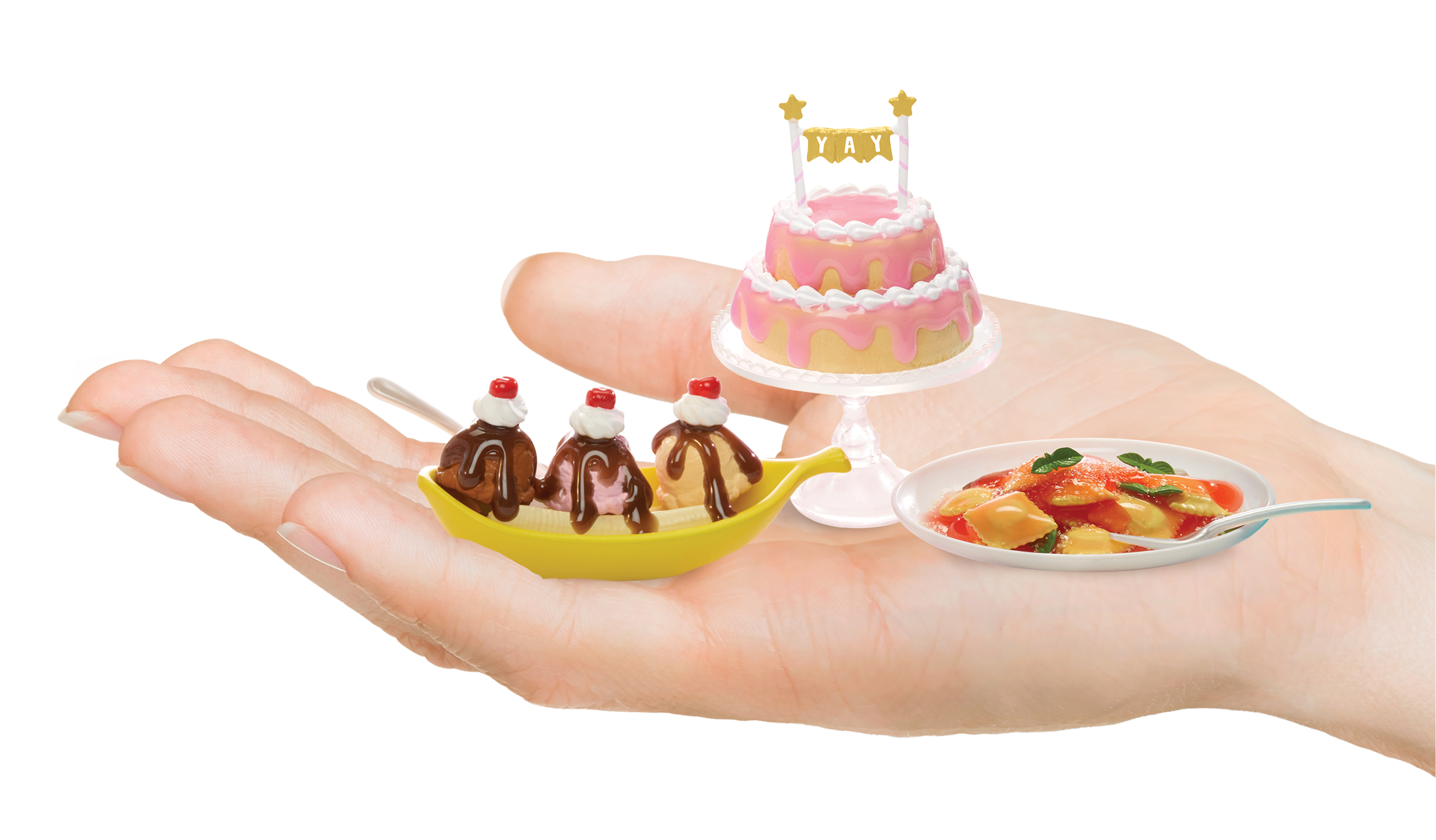 Una mano che tiene cibo giocattolo: un banana split con ciliegie, una torta e un piatto di cibo. Lo sfondo è bianco.