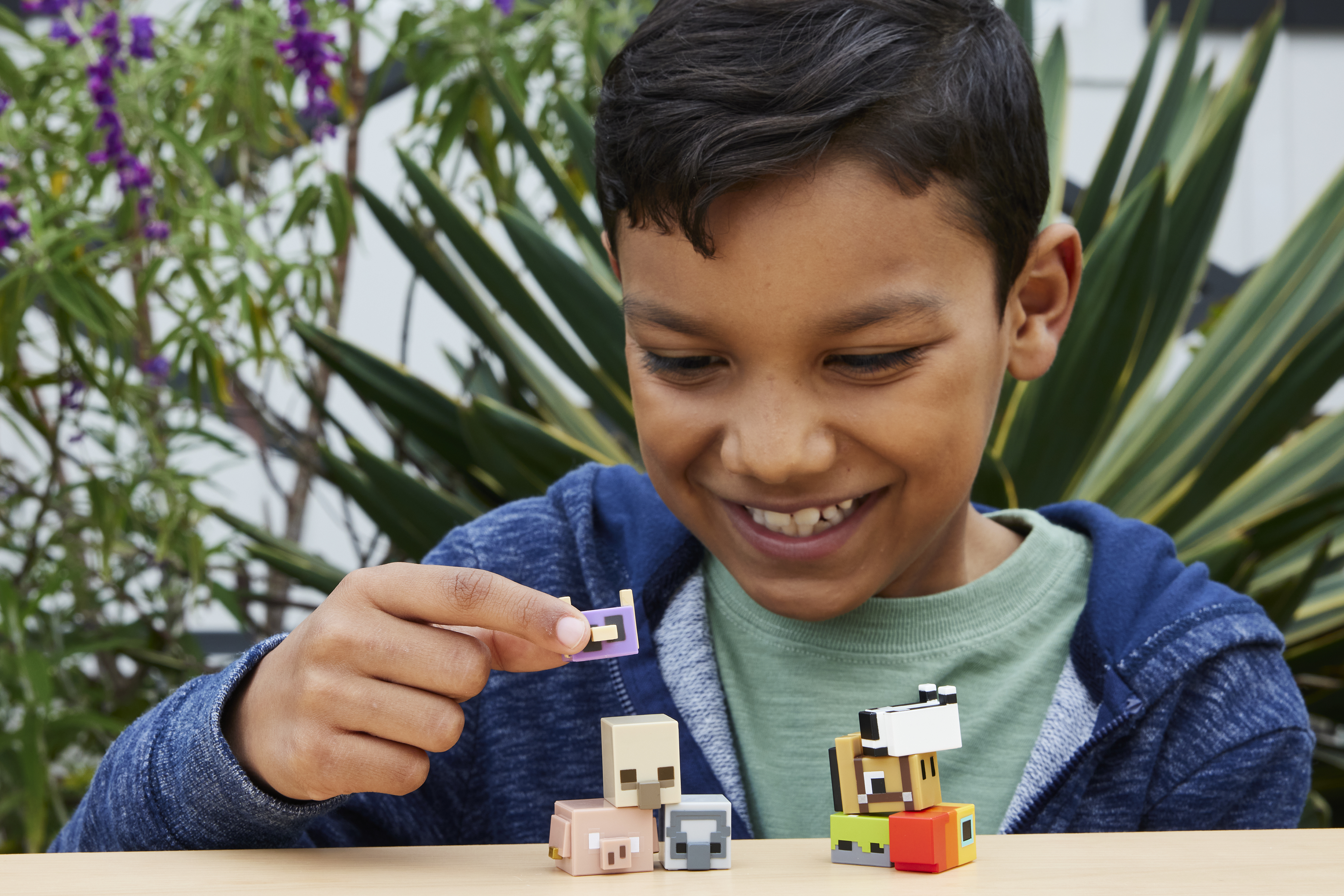 Chłopiec bawiący się figurkami zwierząt z Minecraft. Figurki są na drewnianym stole. Zielone tło.