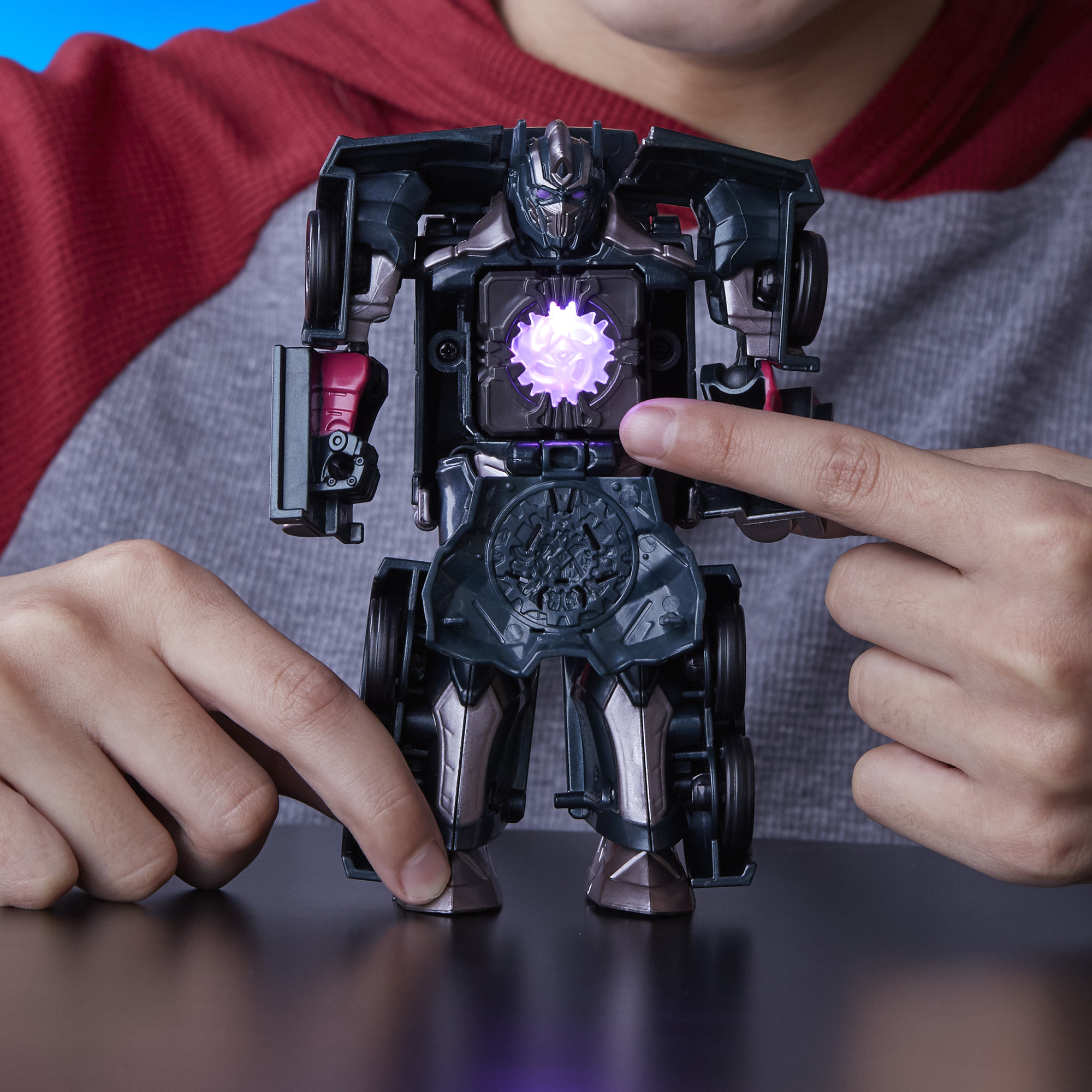 Un ragazzo tiene in mano un giocattolo Transformer. Il giocattolo ha un centro luminoso. Le mani del ragazzo sono visibili.