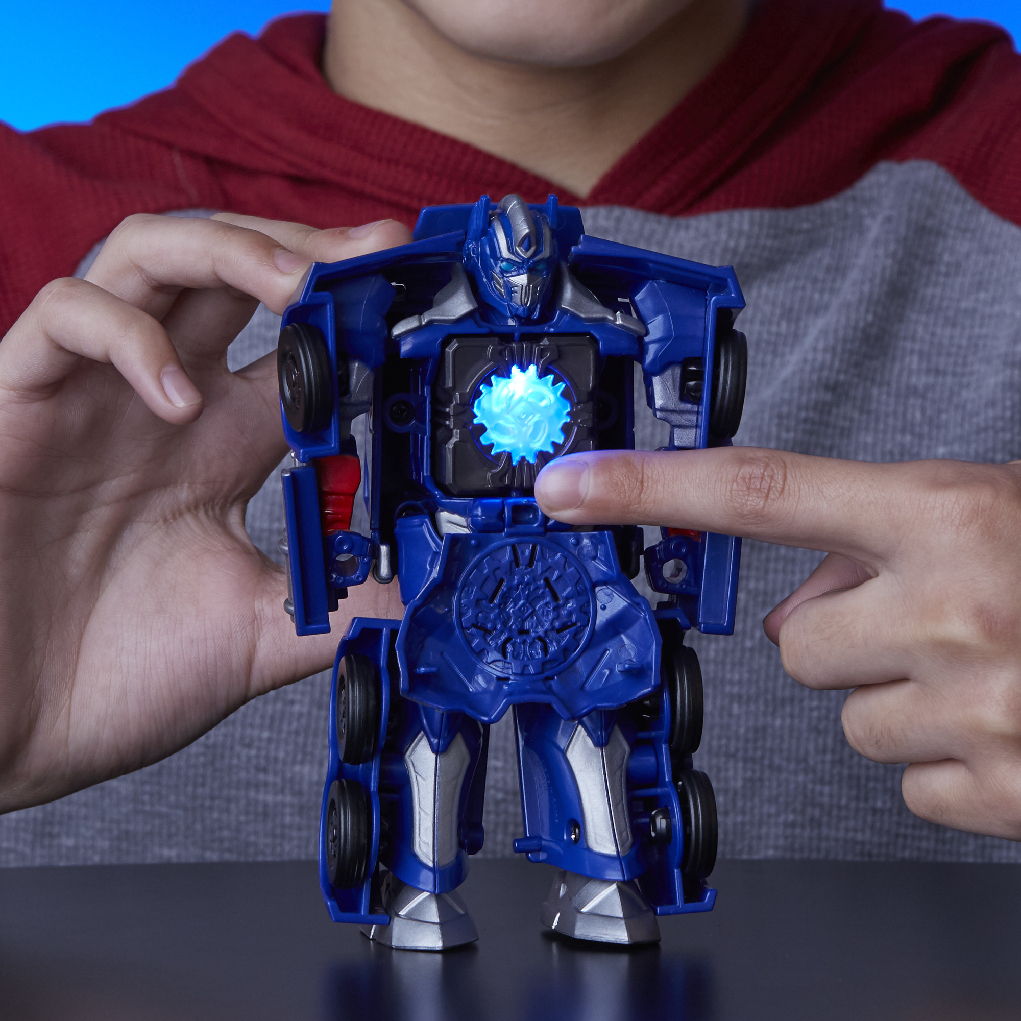 Le mani di un bambino toccano il petto blu di un robot Transformer blu. Il robot ha un centro luminoso.
