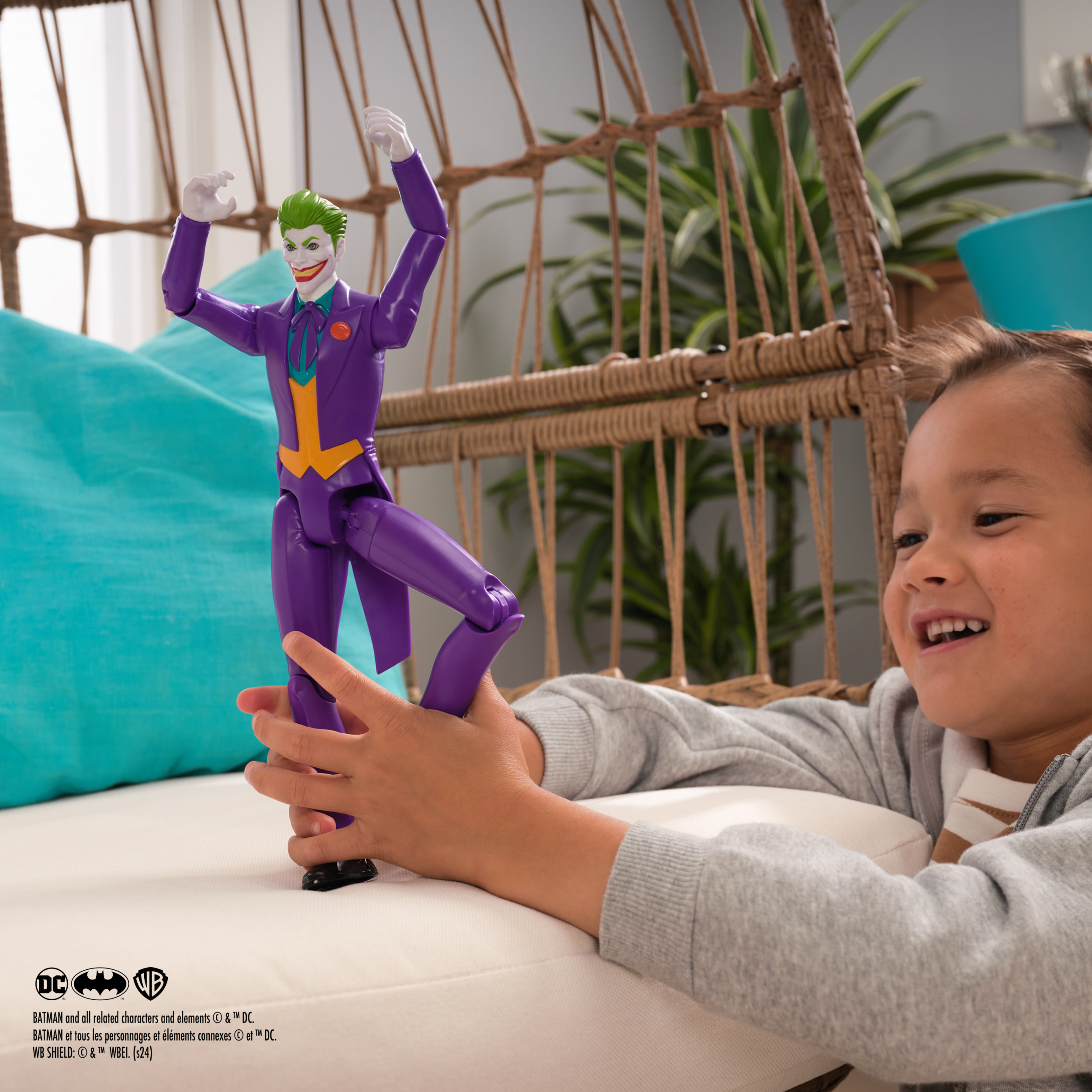 Dziecko bawiące się figurką Jokera w pokoju. Duża figurka Jokera jest w ręce dziecka.