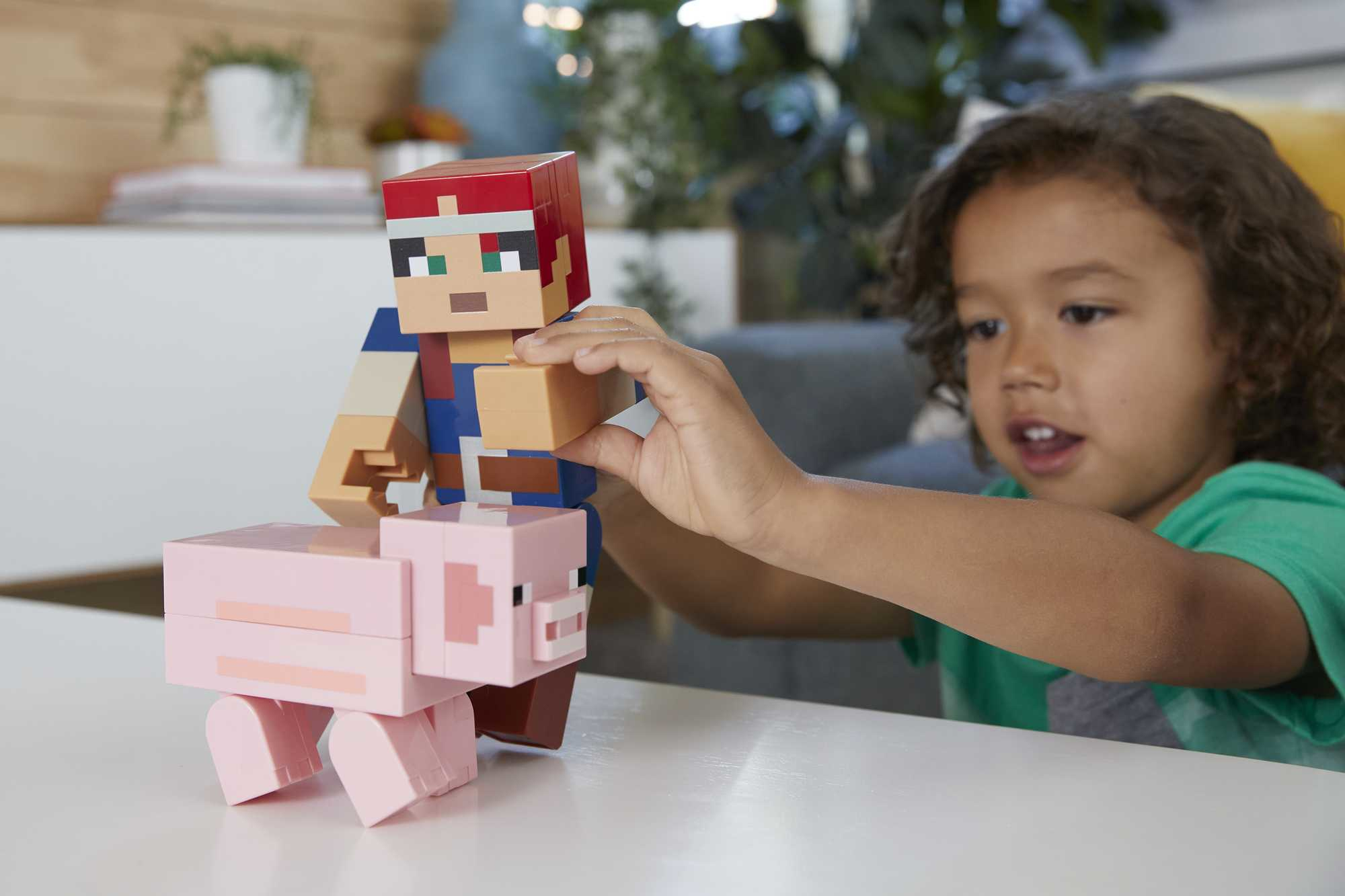 Ein Kind spielt mit Minecraft-Spielzeugen und setzt eine Steve-Figur auf eine rosa Schweinefigur.