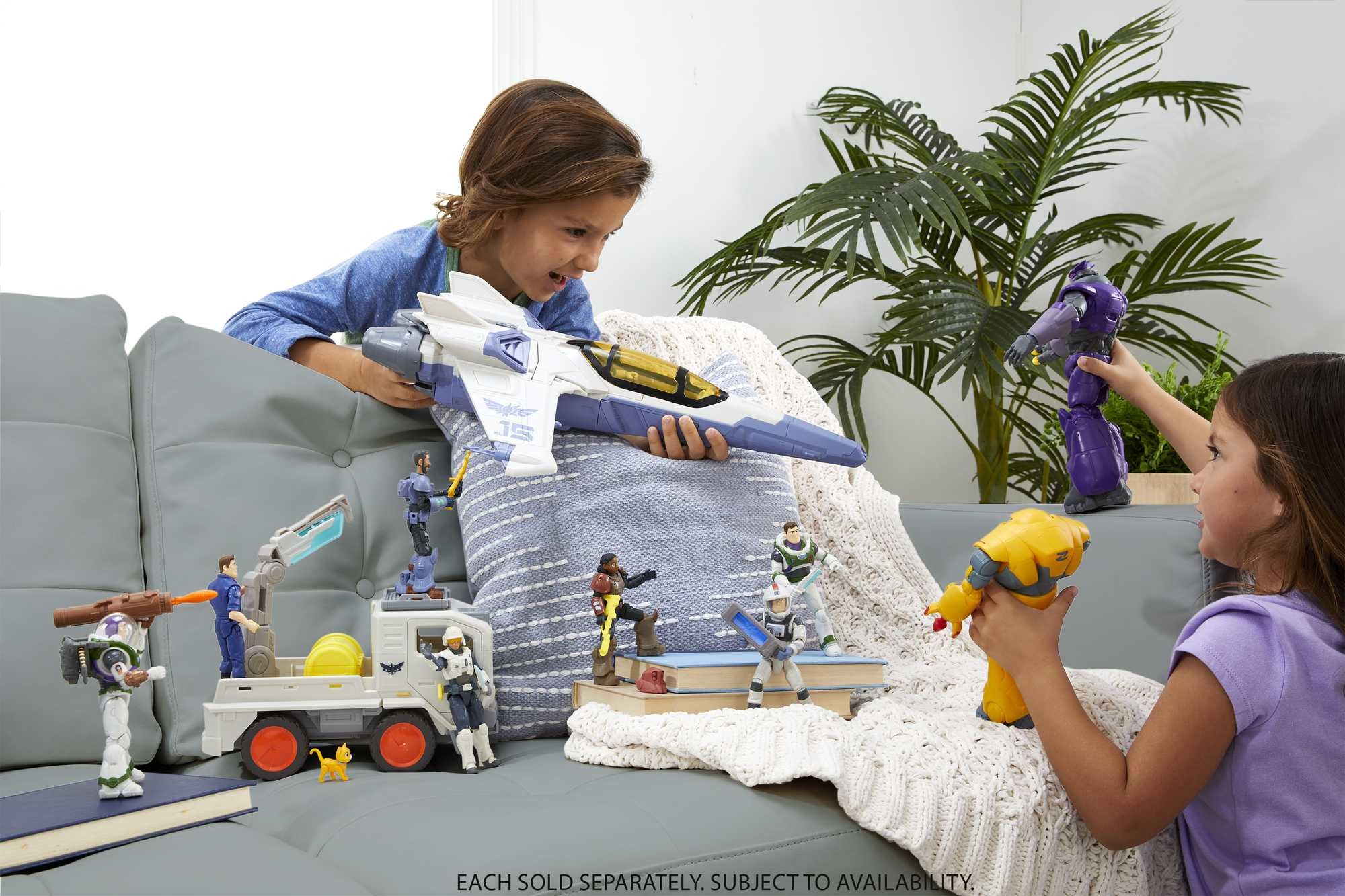 Dwoje dzieci bawiących się figurkami i statkiem kosmicznym. Jedno dziecko patrzy na zabawki. Zabawki są na kanapie.