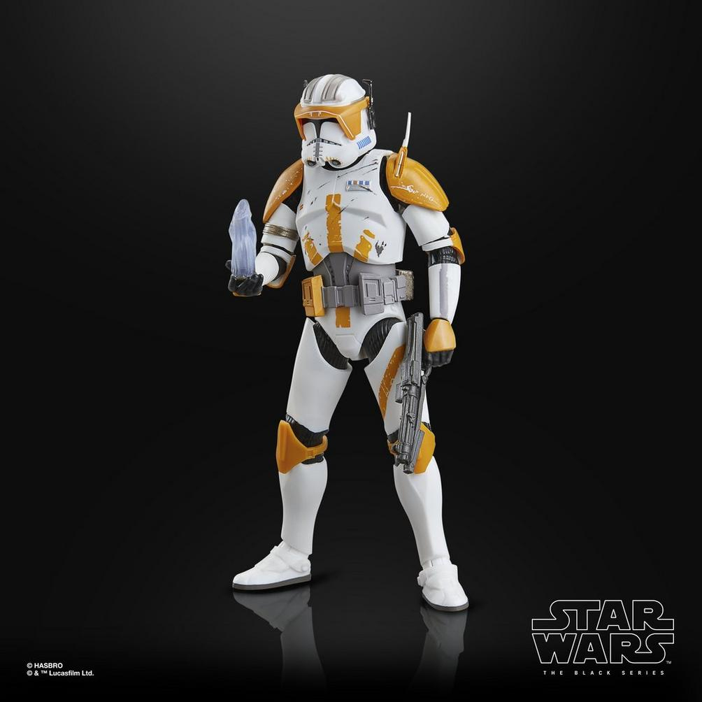 Turuncu detaylı bir Star Wars klon askeri figürü, mavi bir nesne tutuyor, siyah arka plan.