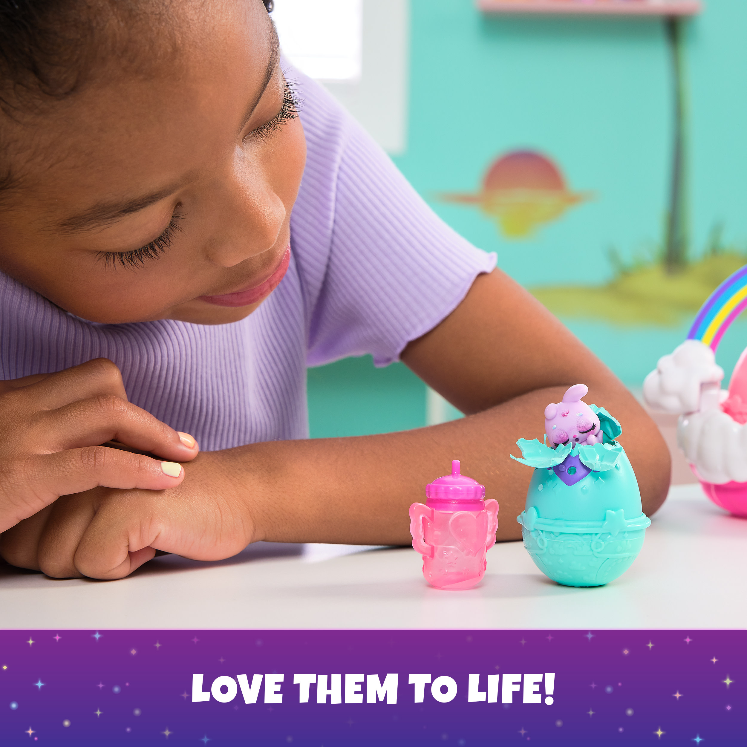 Młoda dziewczyna patrząca na zabawkę dla dziecka wykluwającą się z jajka, obok różowej butelki i tęczy.