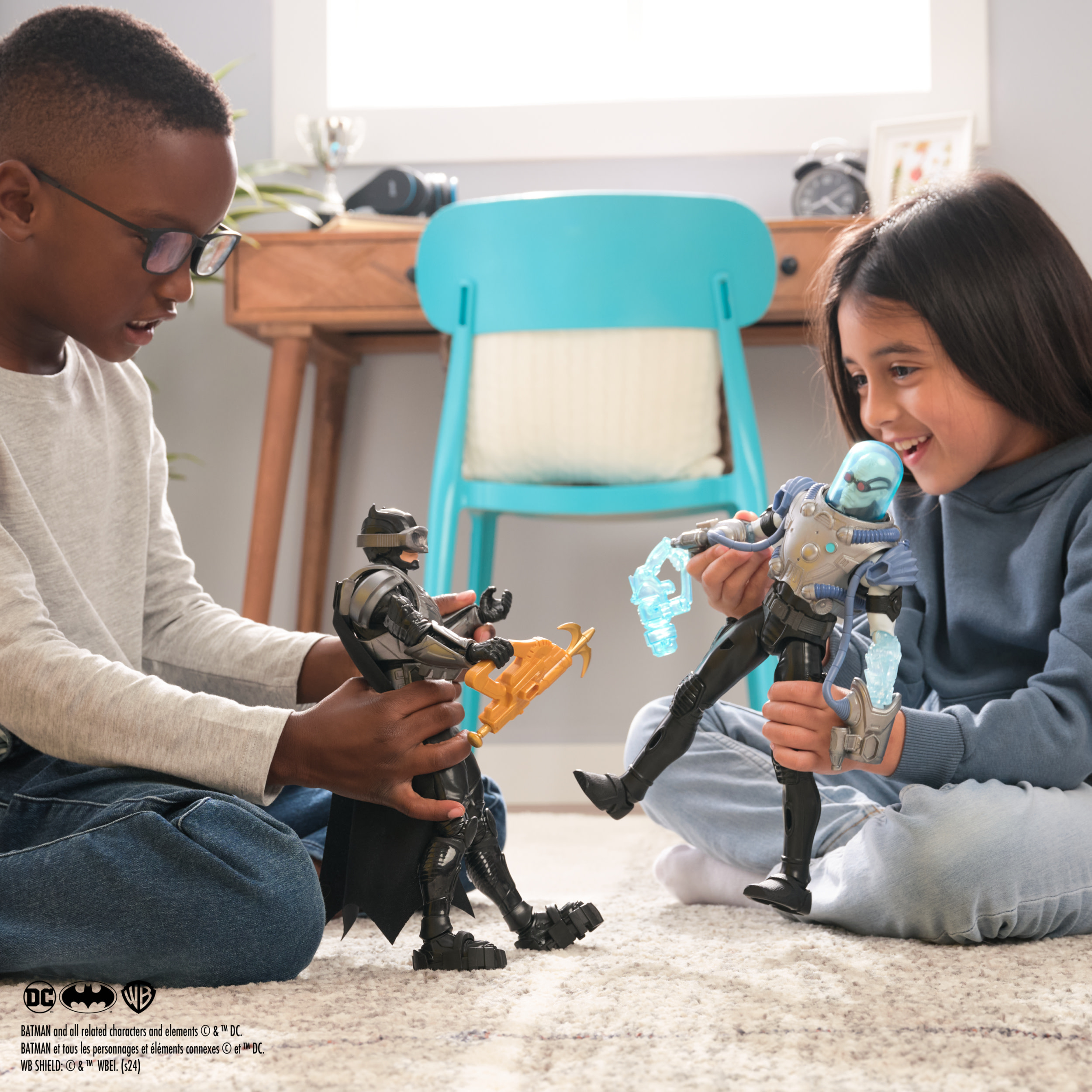 Dwoje dzieci bawi się figurkami Batmana i Mr. Freeze. Tło to wnętrze pokoju.