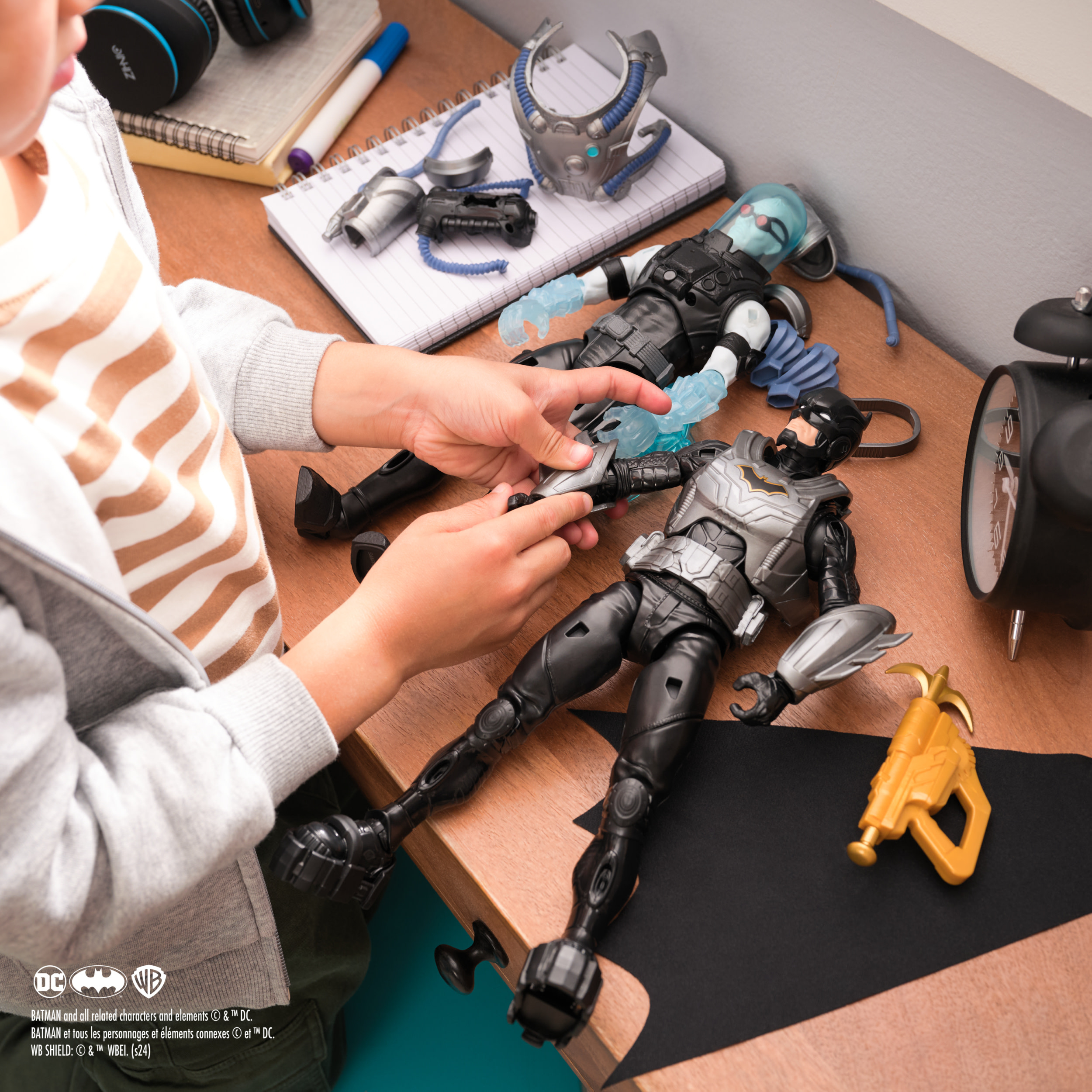 Dziecko bawiące się figurkami Batmana i Mr. Freeze. Przedmioty na biurku, z czarnym płaszczem.