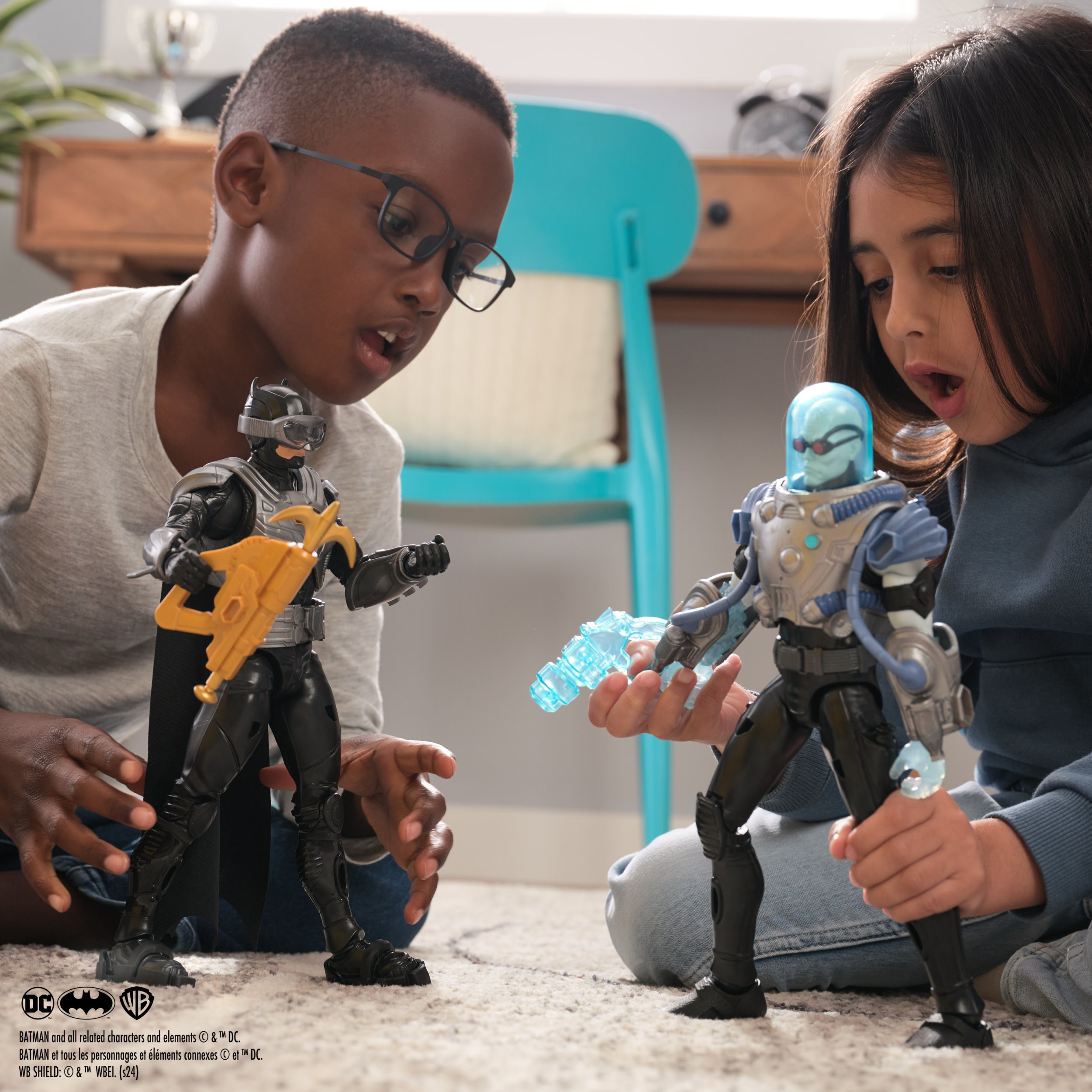 Dwoje dzieci bawi się figurkami Batmana i Mr. Freeze. Tło to wnętrze pokoju.