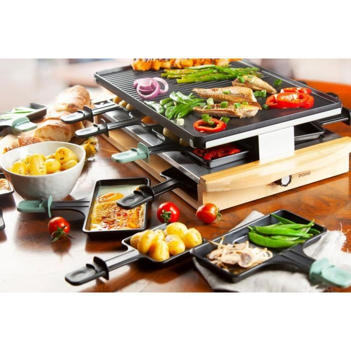 Griglia per raclette con cibo. Formaggio, patate, verdure e carne sono sulla griglia e sui vassoi.