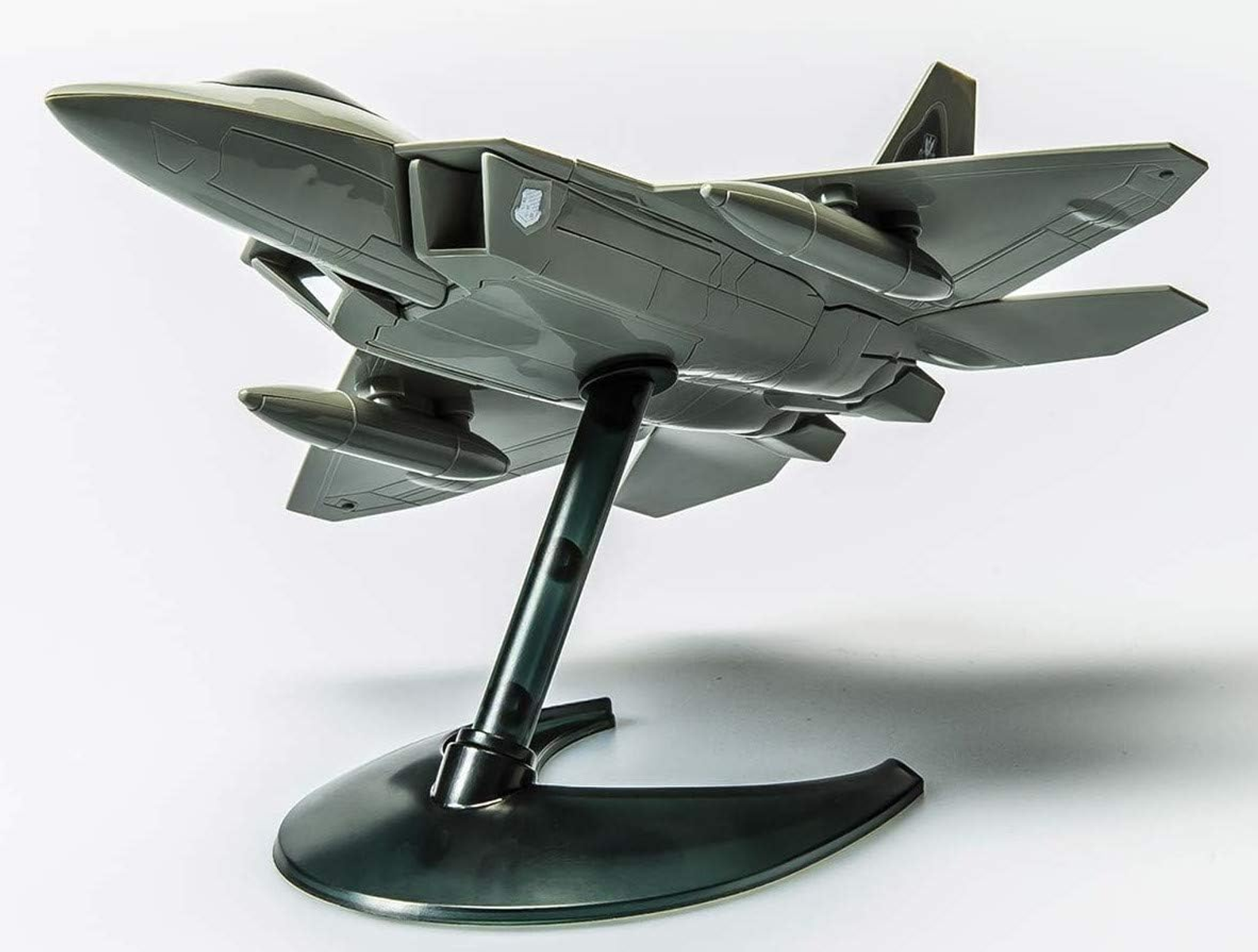 Szary model F-22 Raptor na podstawce. Model jest skierowany w górę, na białym tle.
