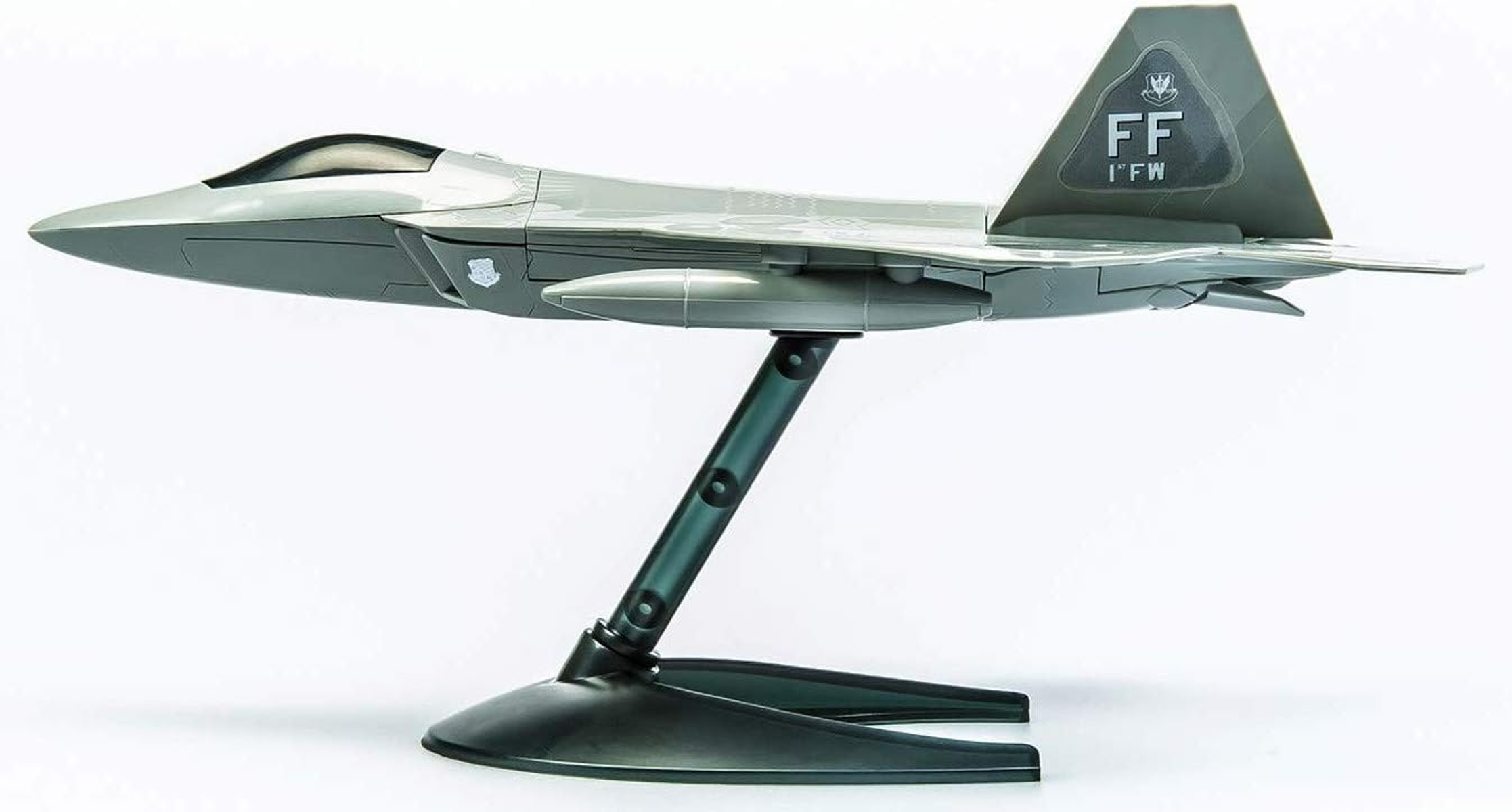 Szary model F-22 Raptor na podstawce, widok z boku. Znajduje się na białym tle.