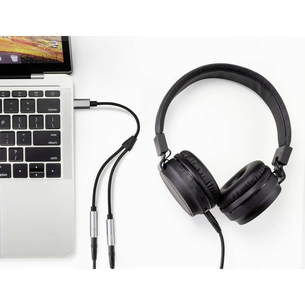 Un laptop collegato a uno sdoppiatore per cuffie e cuffie nere su una superficie bianca.