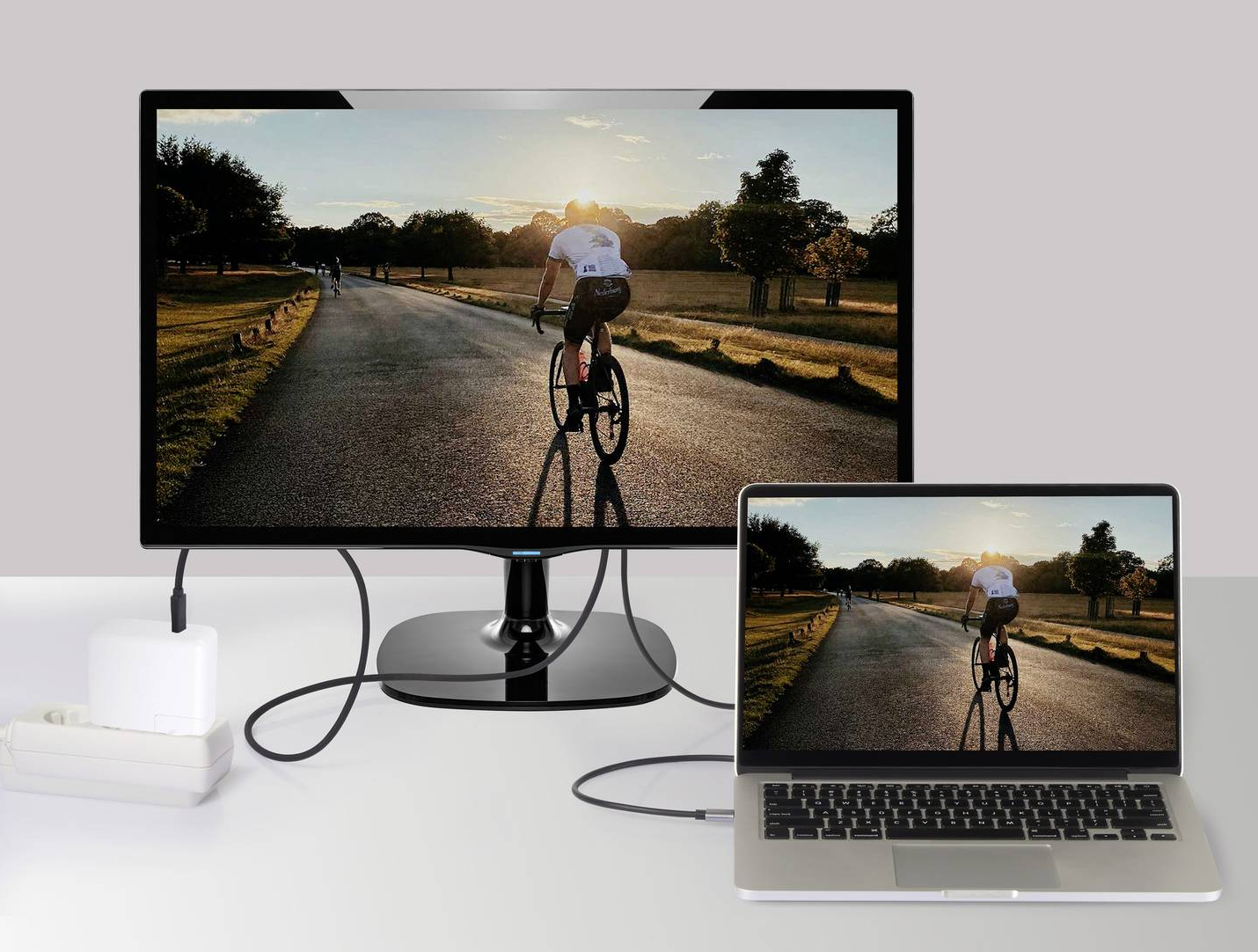 Un laptop e un monitor che mostrano un ciclista su una strada, collegati con cavi.
