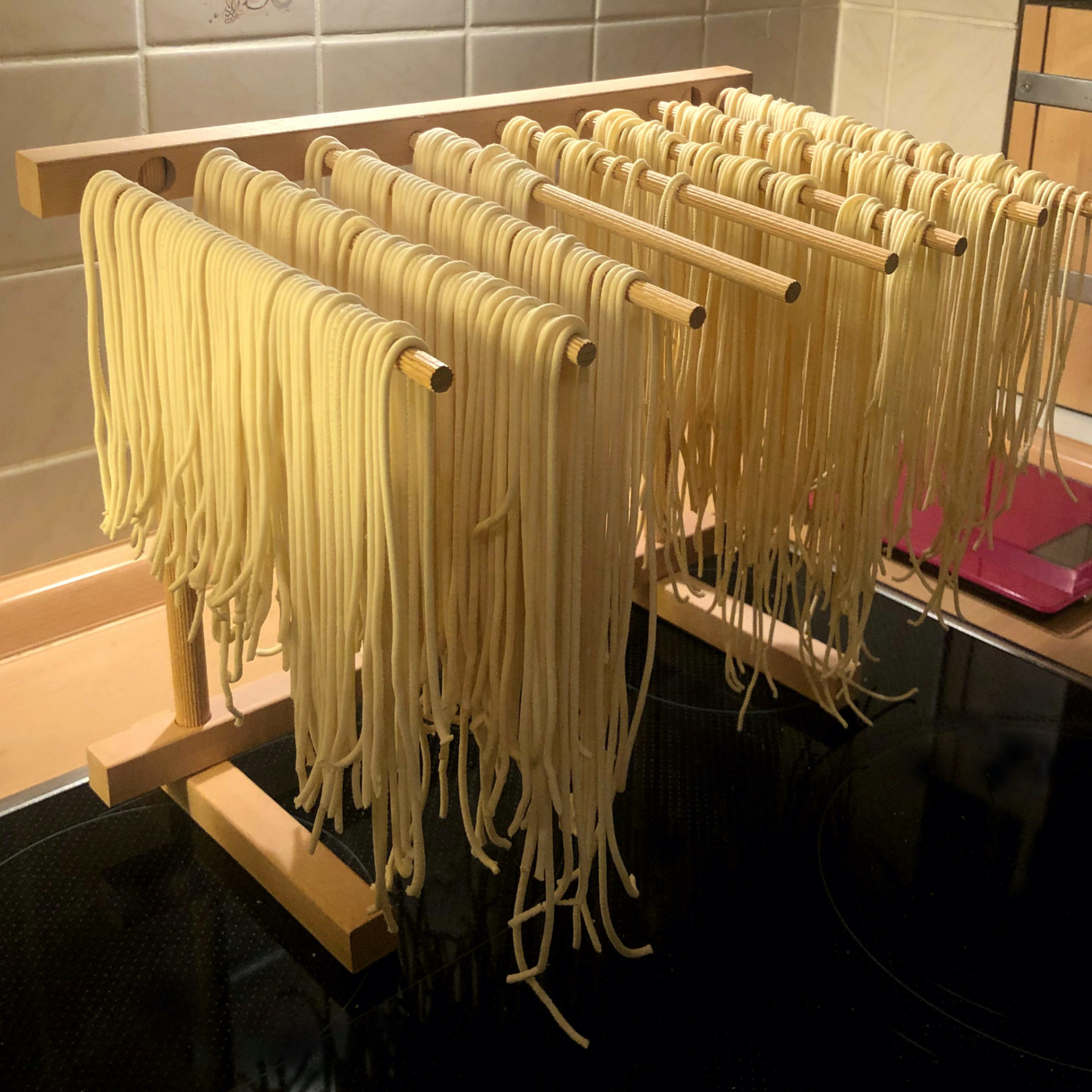 Nudeltrockner aus Holz mit langer, frischer Pasta. Holz- und schwarze Oberfläche.