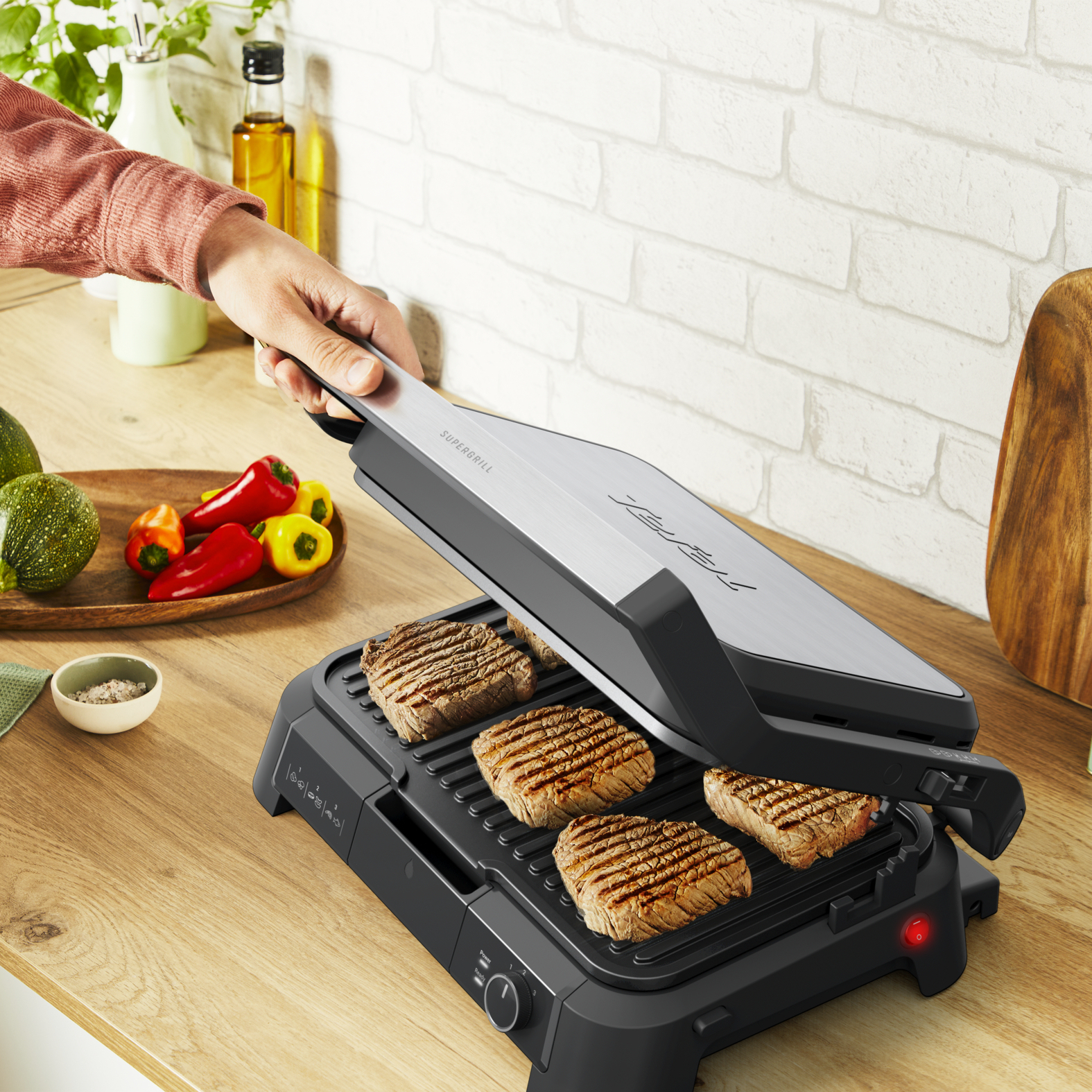 Eine Person grillt Steaks auf einem schwarzen Grill, mit Gemüse daneben.