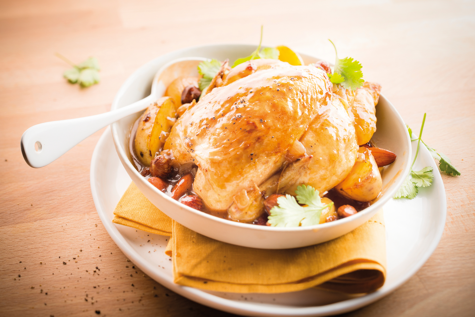 Hähnchen in einer Schüssel mit Kartoffeln, Soße und Mandeln. Gelbe Serviette. Holztisch.