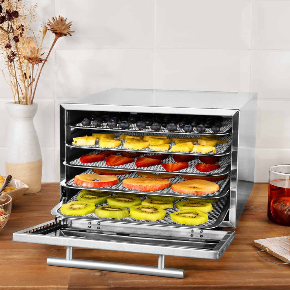 Lebensmitteltrockner mit offener Tür. Aufgeschnittene Früchte auf Tabletts. Holztisch.
