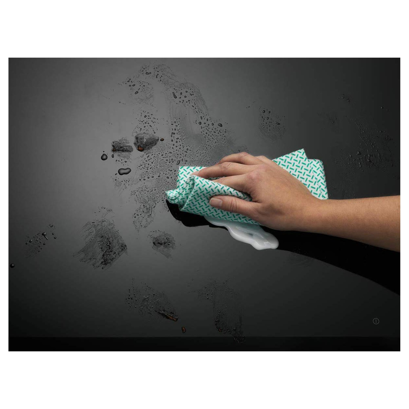 Ręka osoby wyciera błyszczącą czarną powierzchnię zielono-białą wzorzystą szmatką.