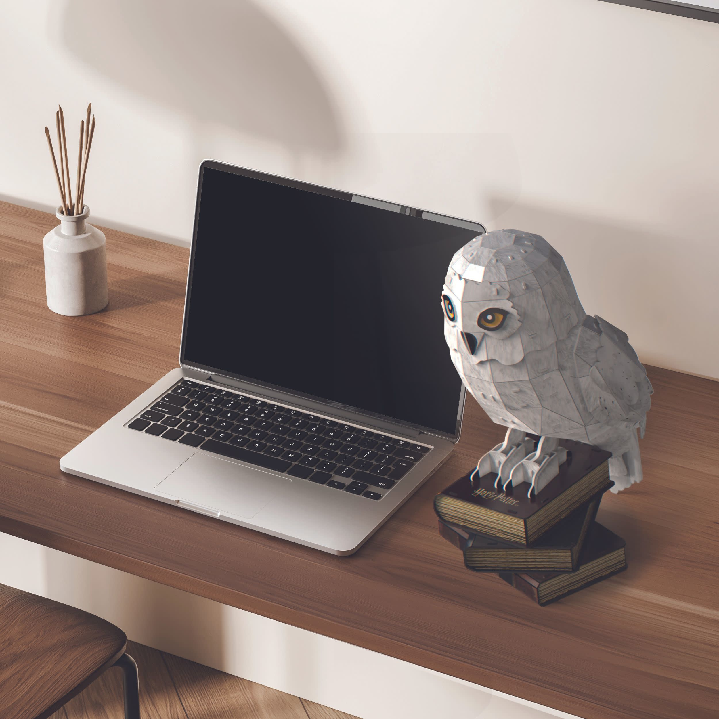 Laptop i papierowa układanka z sową na drewnianym stole. Sowa ma żółte oczy.