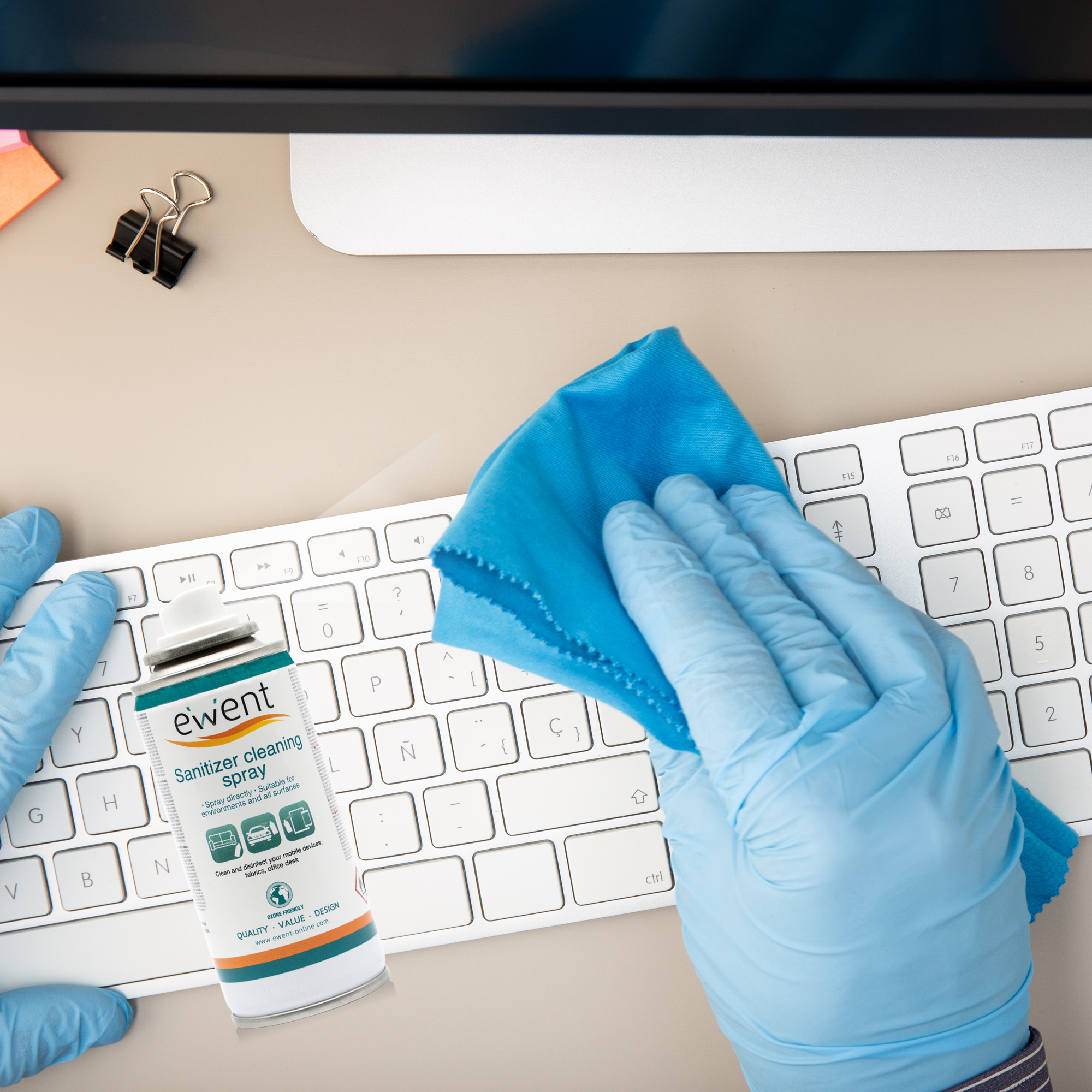 Osoba w rękawicach dezynfekująca klawiaturę za pomocą sprayu i szmatki.