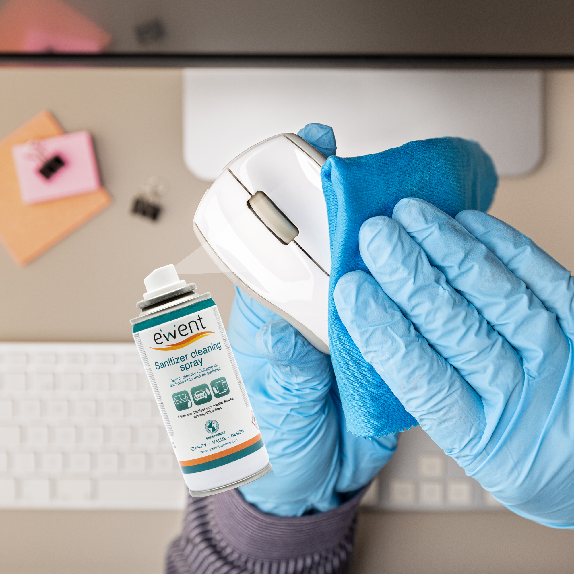 Ręka w rękawicy czyści białą mysz komputerową za pomocą sprayu dezynfekującego.