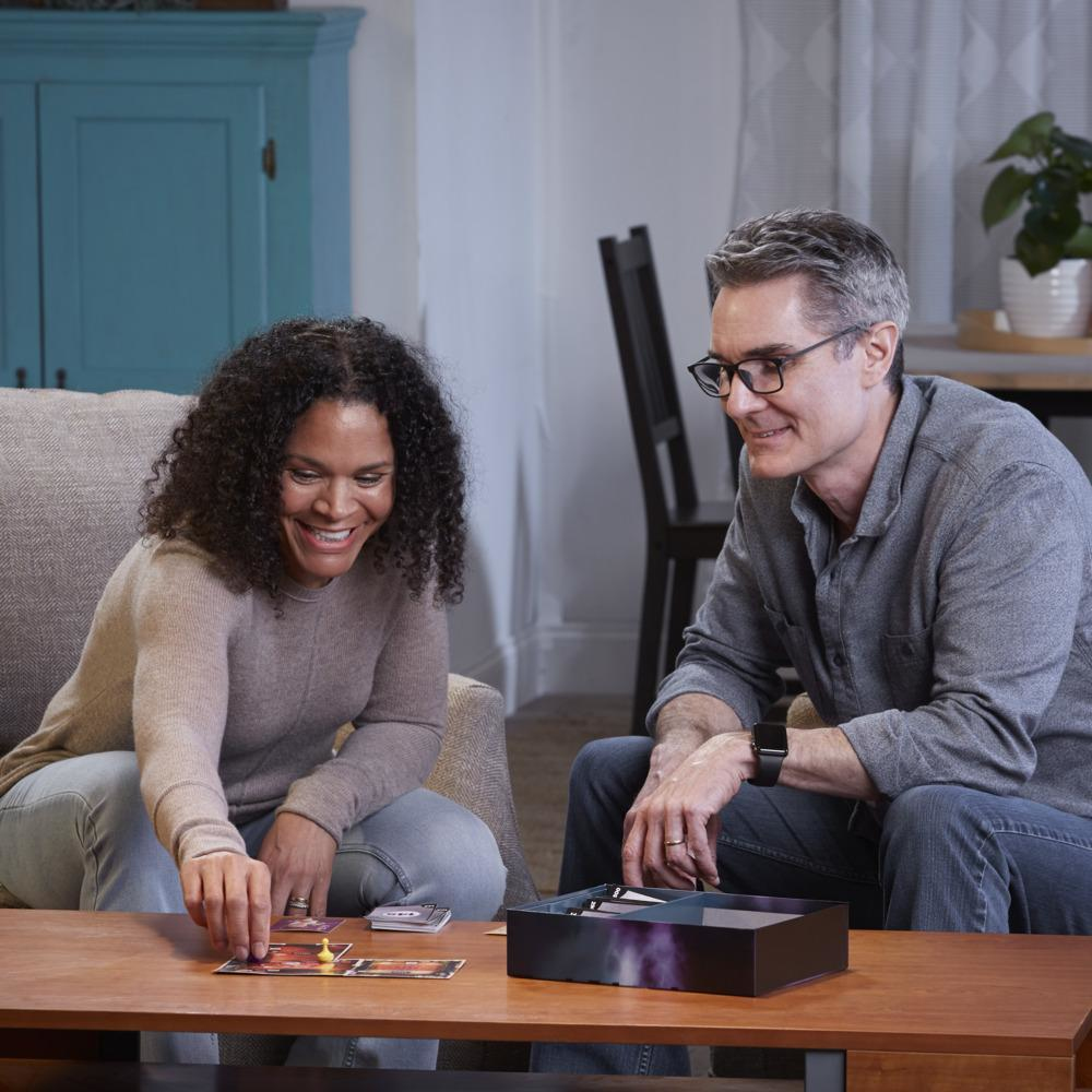 Twee mensen spelen een bordspel aan een houten tafel in een woonkamer.